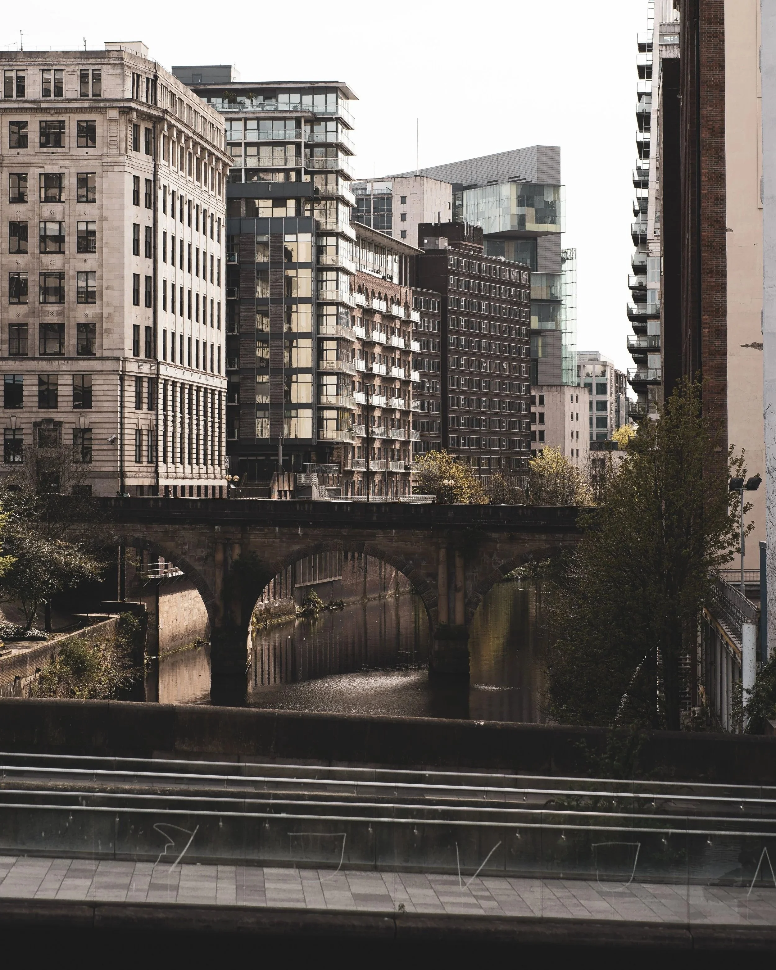 View of modern and historic buildings along a city canal with a bridge beneath, photographed through a glass window with reflections.