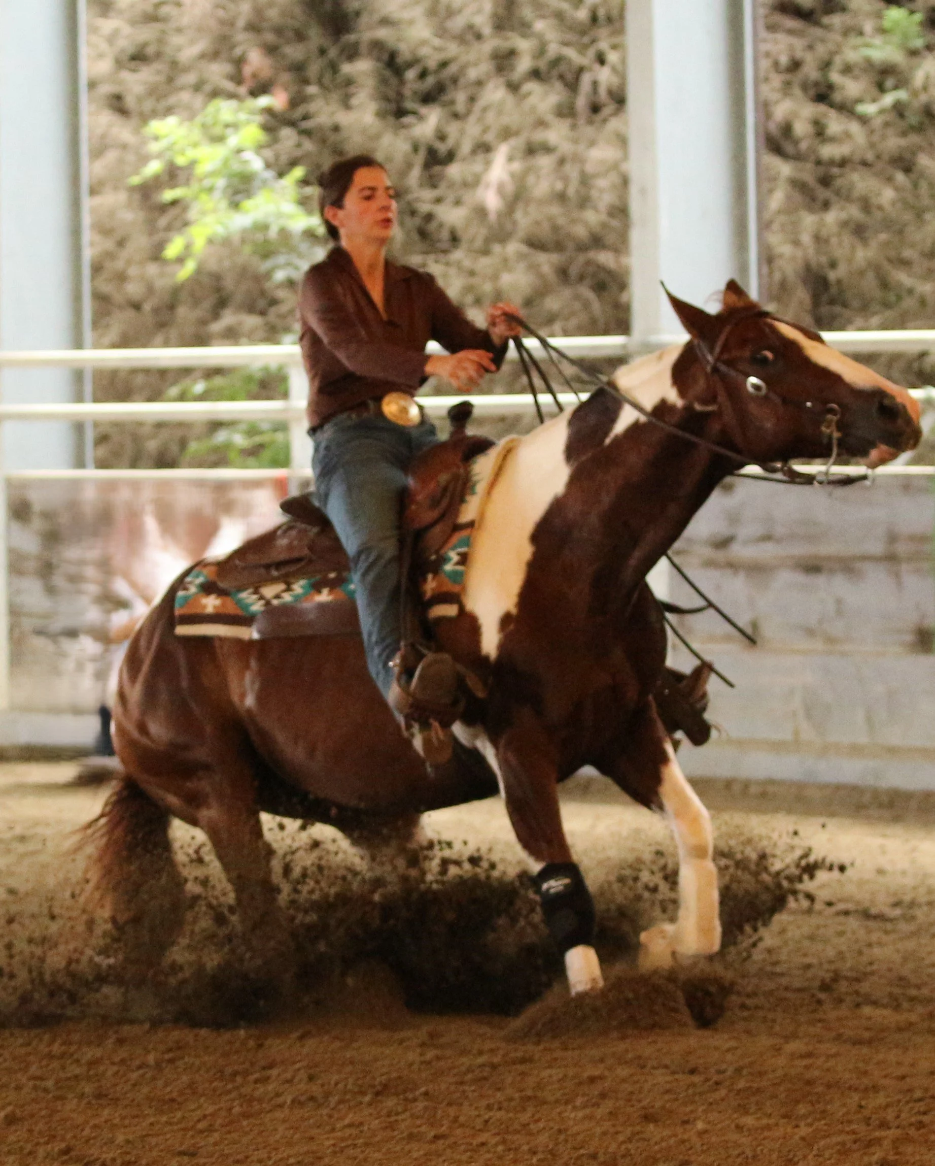A woman riding a horse in an indoor arena with a dirt floor and a rocky background.