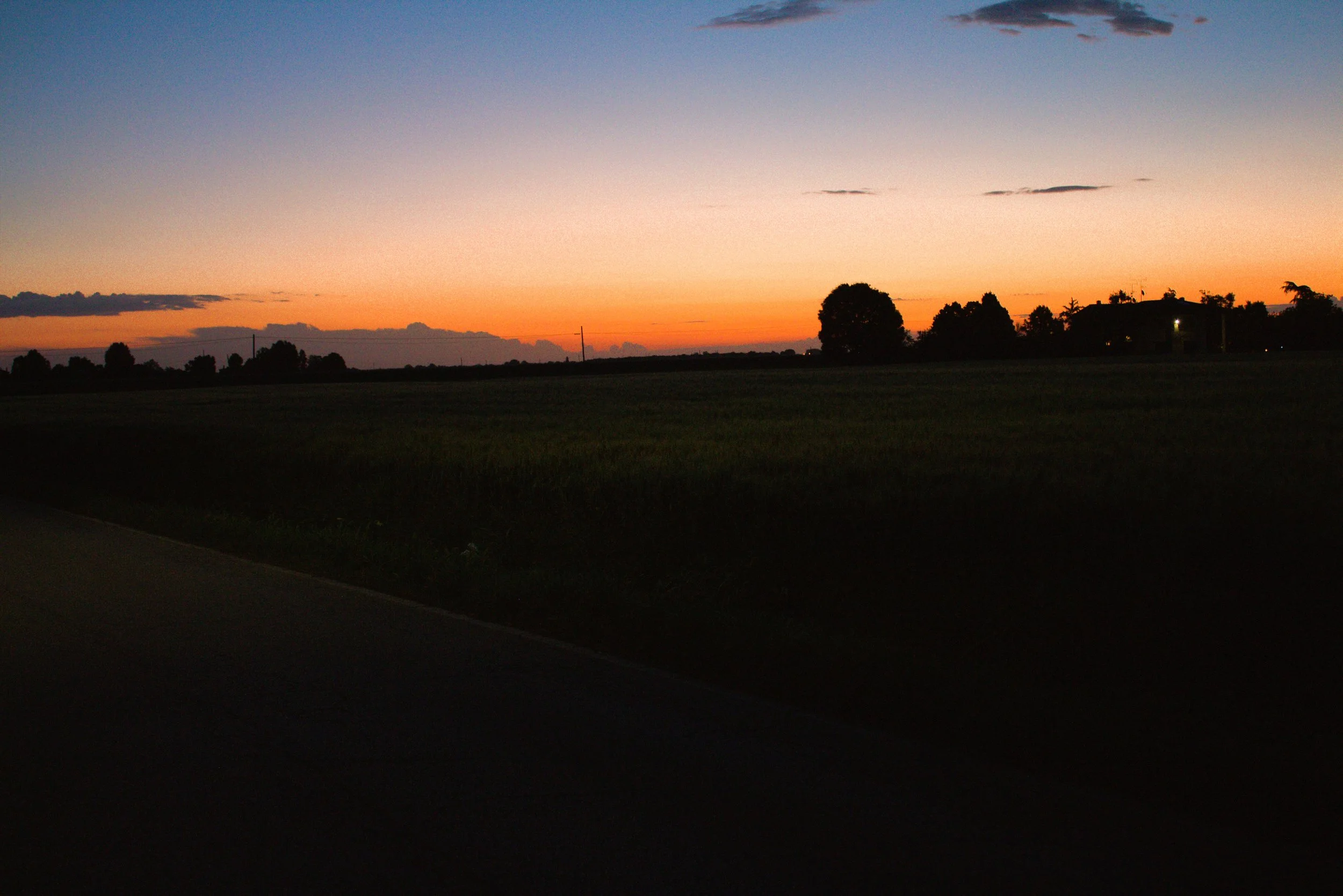 A landscape view of a sunset sky with shades of pink, orange, and purple, and silhouettes of trees and buildings in the distance.