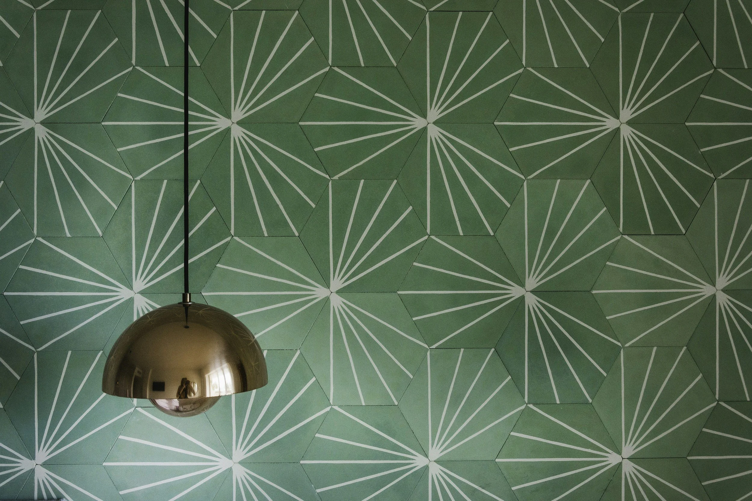 Green tiled ceiling with a geometric pattern and a shiny metallic pendant light hanging down.
