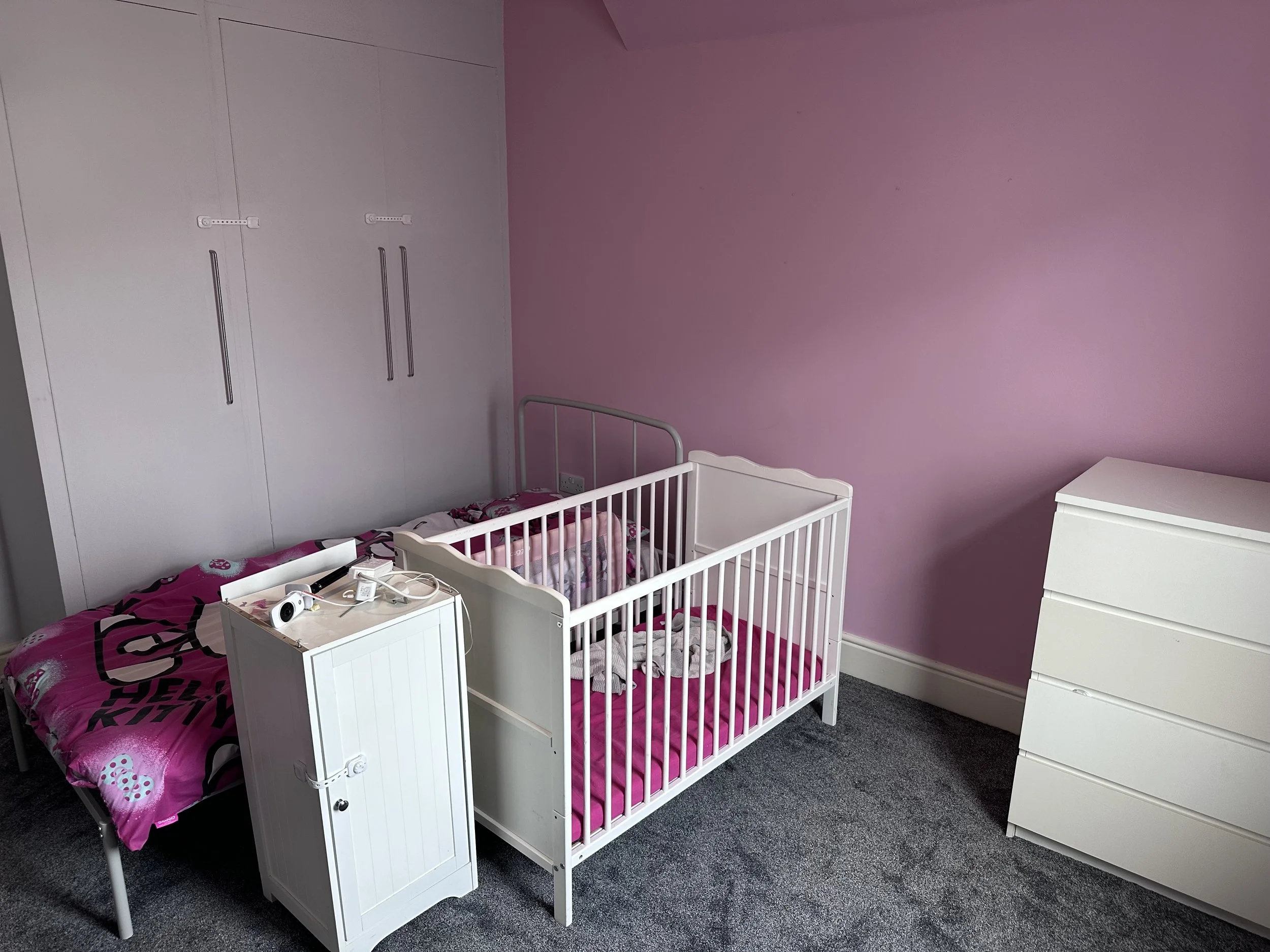 A baby's crib and a bed in a pediatric room with pink and purple walls.