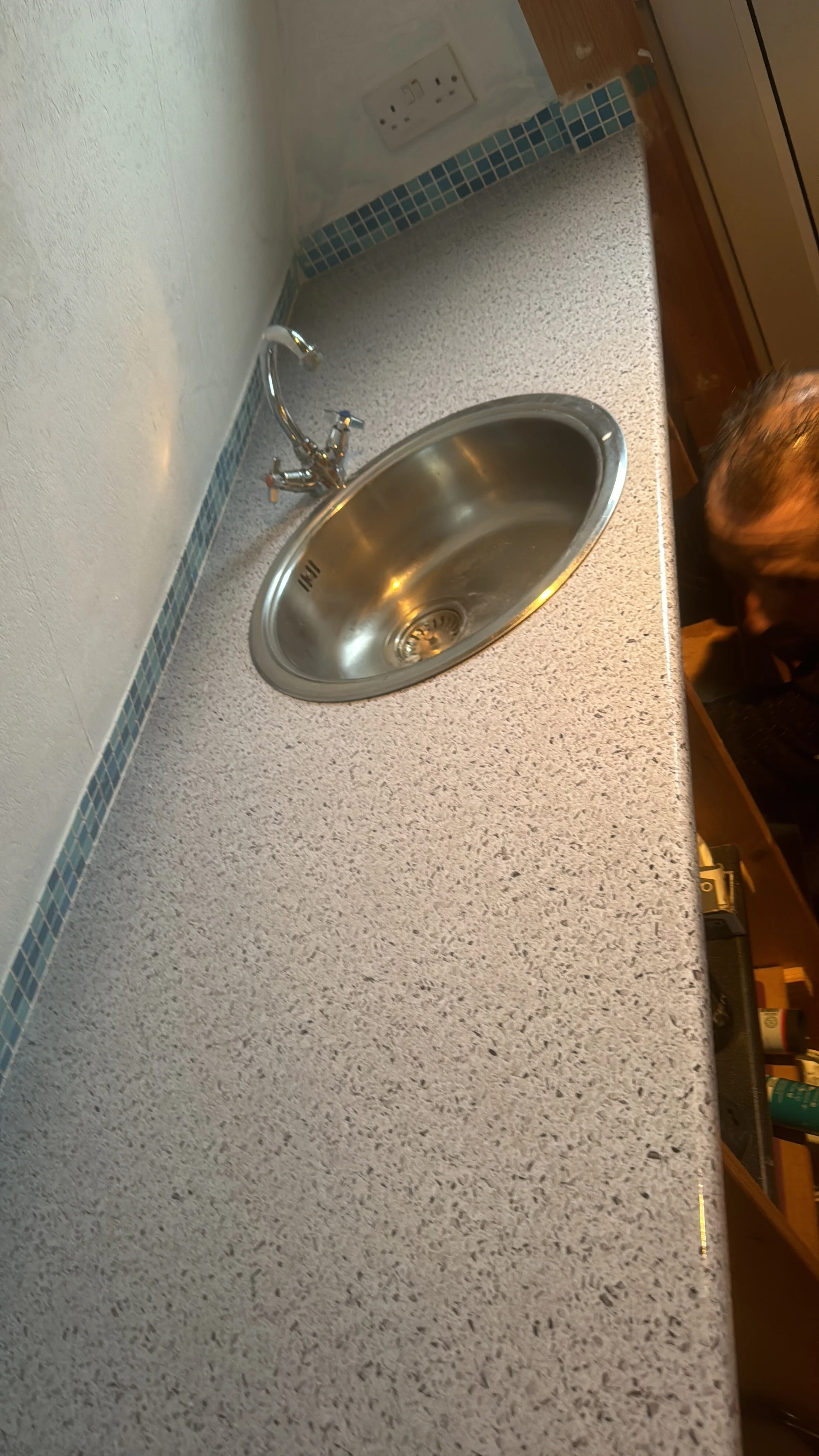 A kitchen countertop with a stainless steel sink and a chrome faucet. An electrical outlet is visible on the wall above the counter.