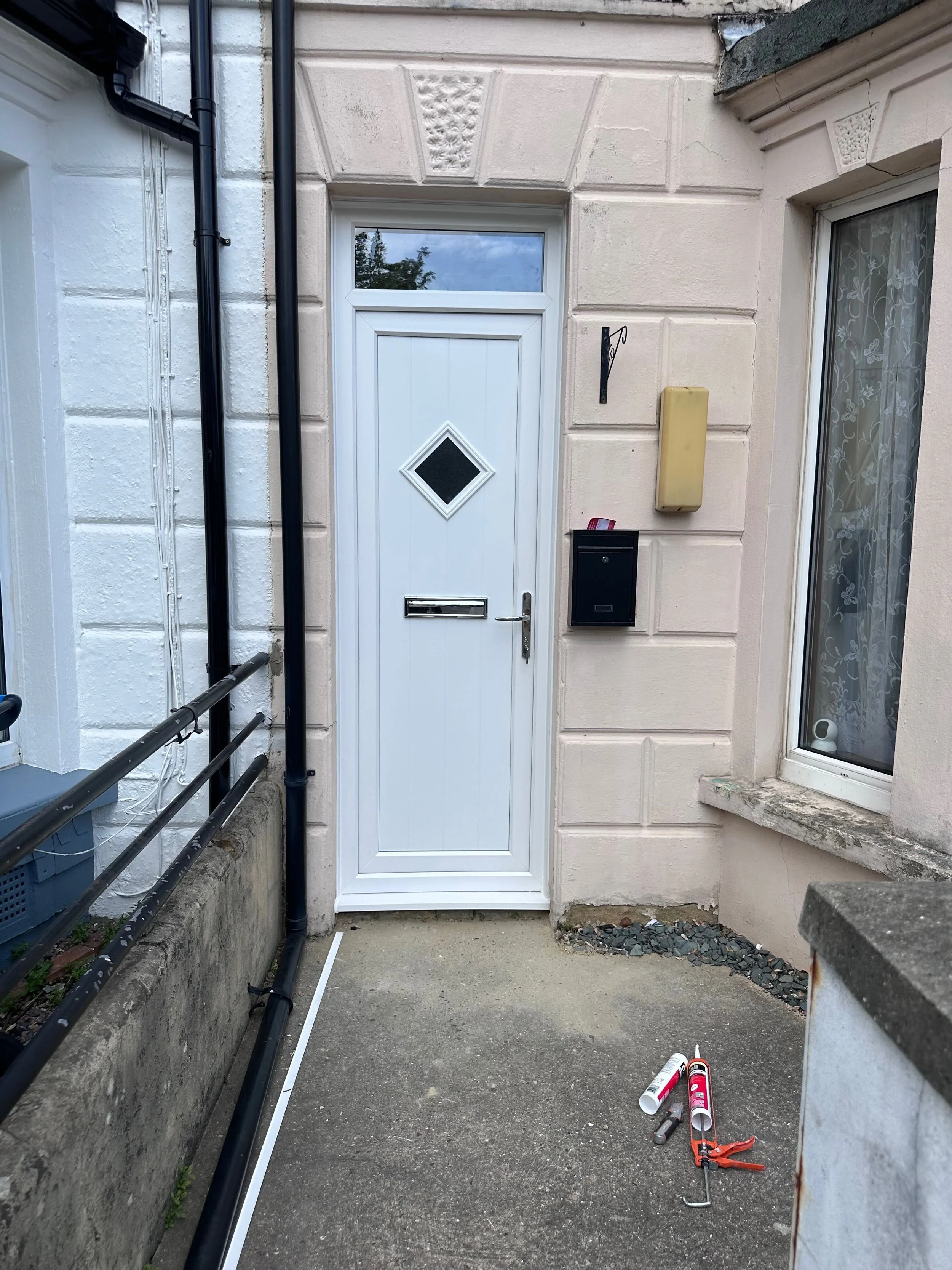 Front door and entranceway of a house under maintenance, with black drainpipes, caulking tubes, and tools on the ground.