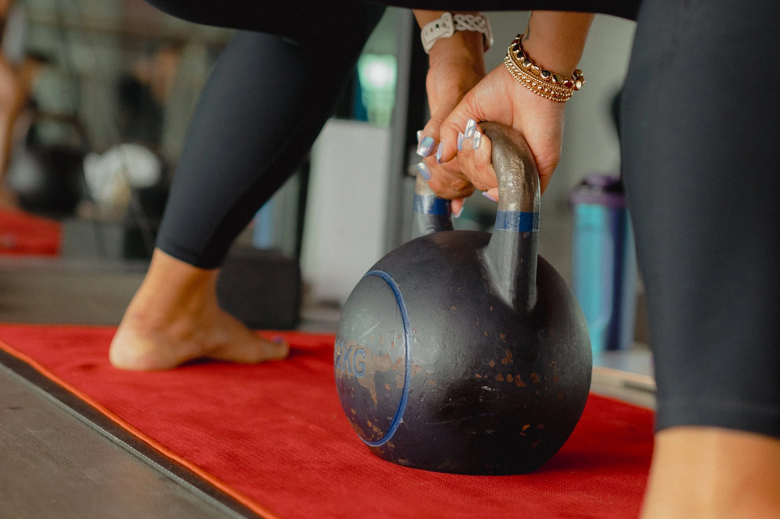 Close-up of a person lifting a kettlebell during a workout on a red exercise mat.
