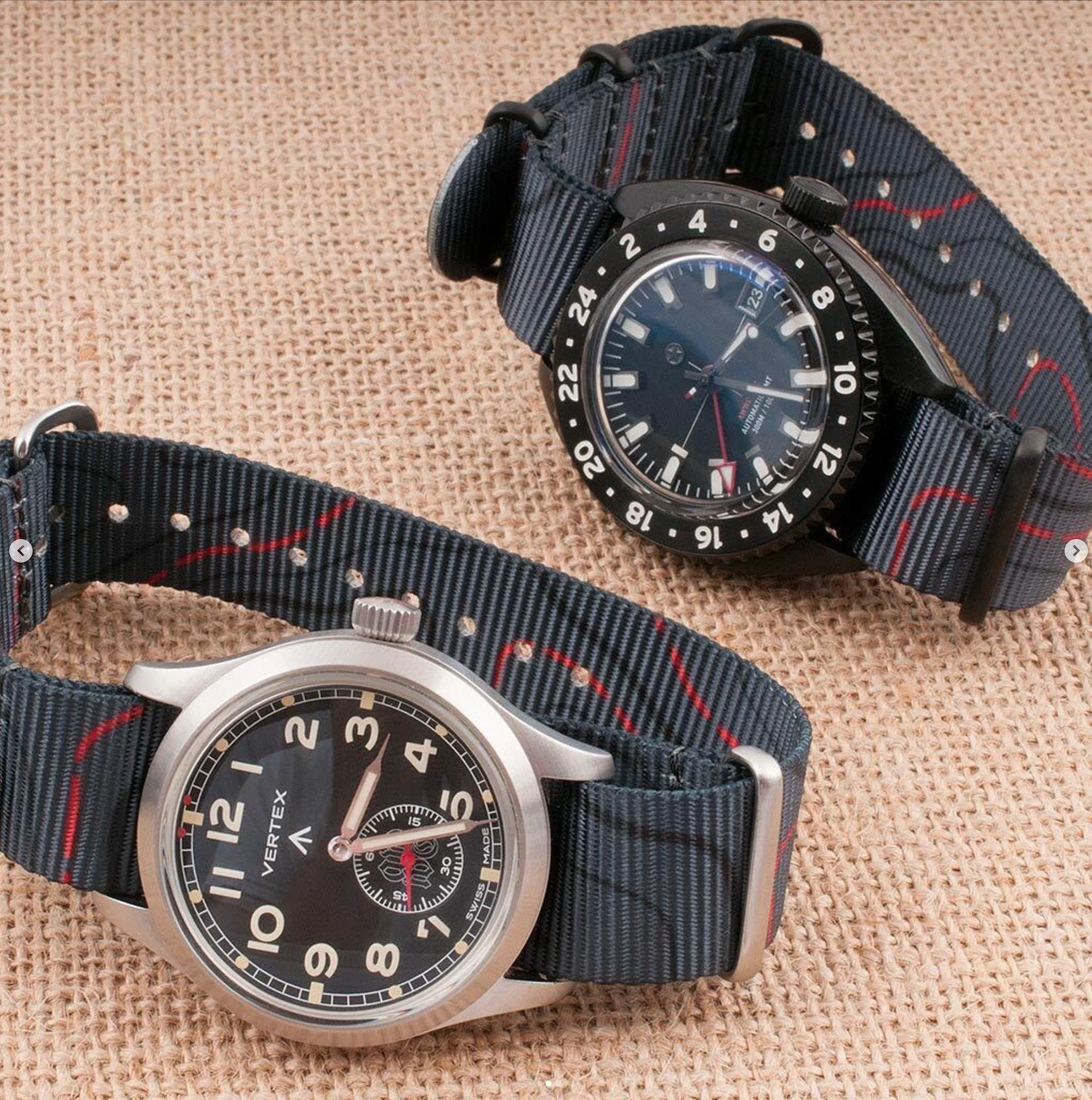 Close-up of two wristwatches with fabric straps, placed on a woven surface. The watches display analog dials with various features.