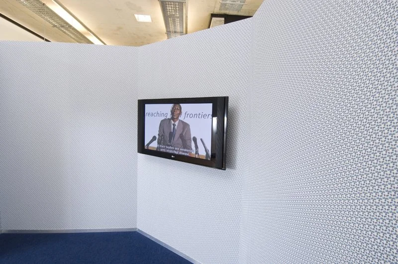 Reaching new frontiers, installation view. Flat-screen monitor, video, sound, wood, metal frame, wallpaper, solution-dyed nylon office carpet, petroleum wax. Installation dimensions variable, 2008
