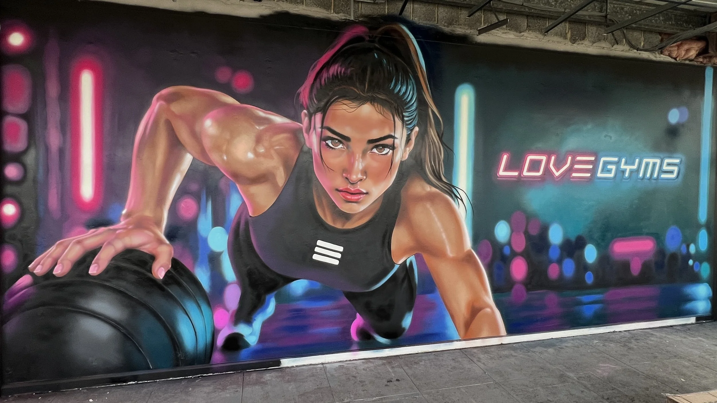 A vibrant mural of a fit woman with dark hair in a ponytail, wearing a black workout top, pushing a large black tire at a neon-lit gym, with the words "LOVE GYMS" in bright pink and blue.