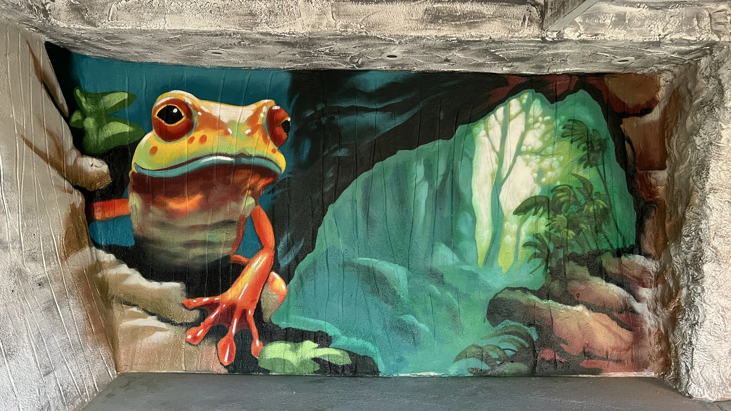 Colorful mural of a frog on a rock, with lush green foliage and rocks in the background.