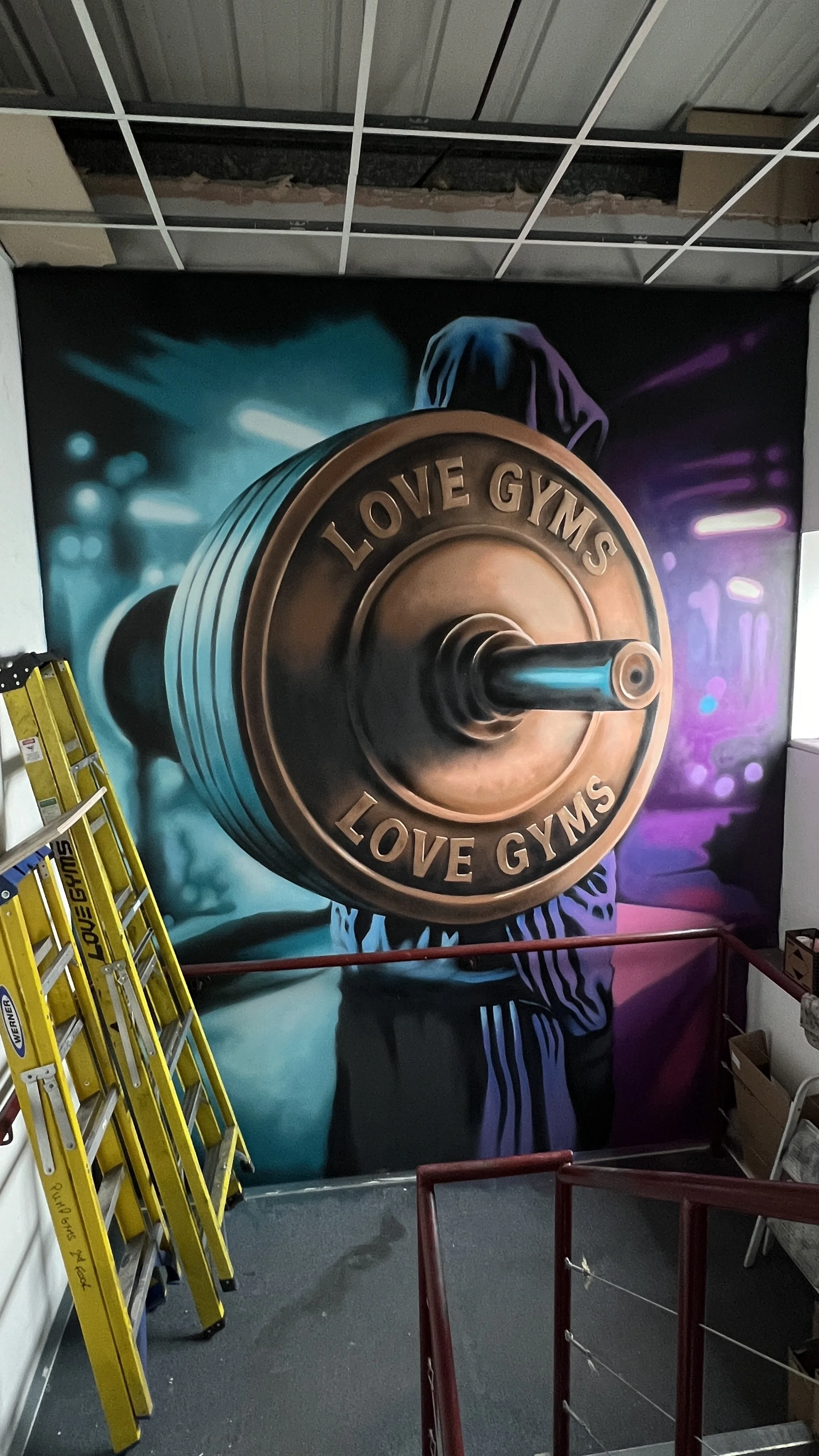 Interior wall with a large mural of a person holding a barbell, with the words "LOVE GYMS" inscribed on the barbell.