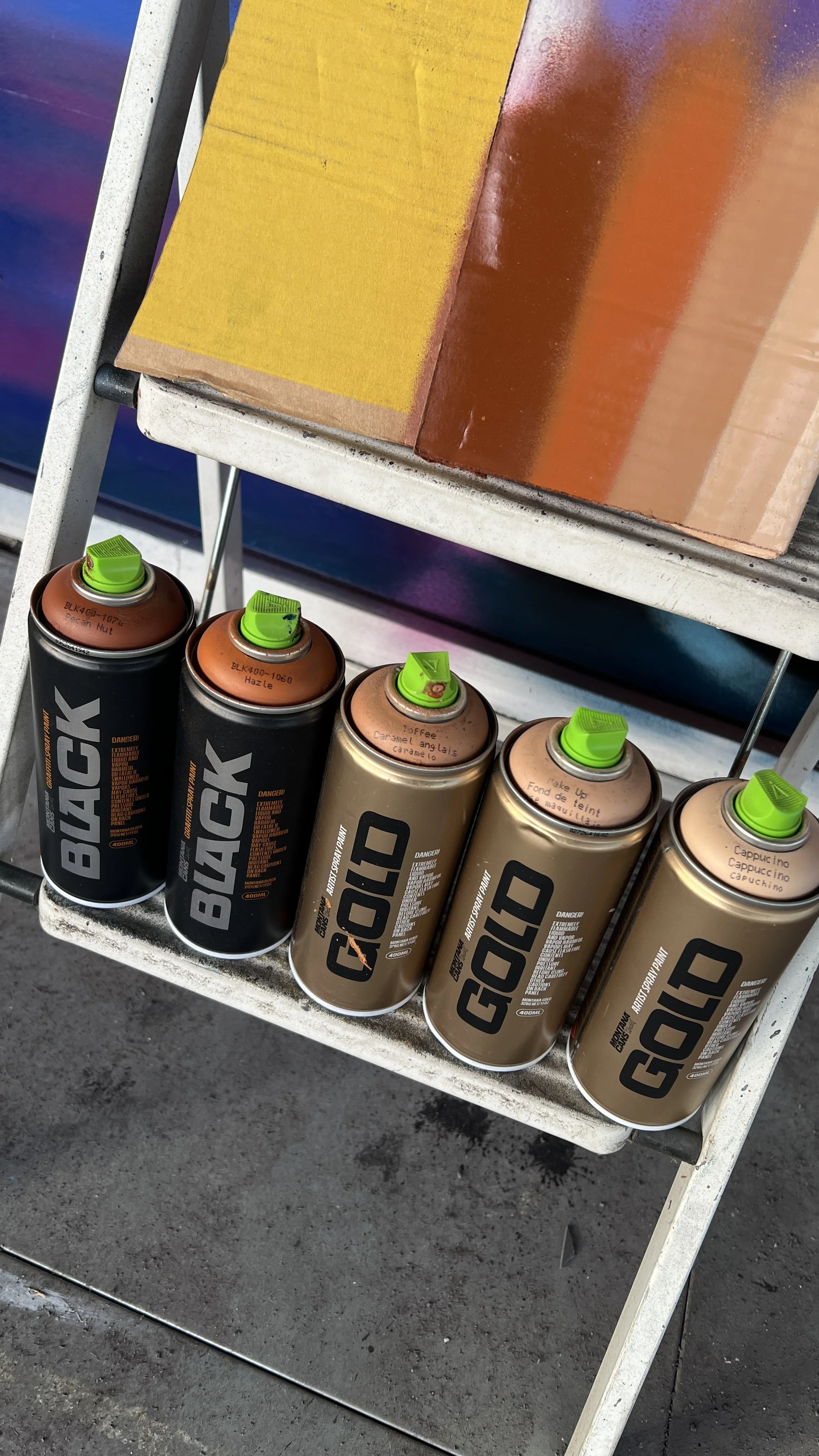 Four cans of G.O.A.T. brand spray paint on a metal cart, with a yellow and orange box above them.