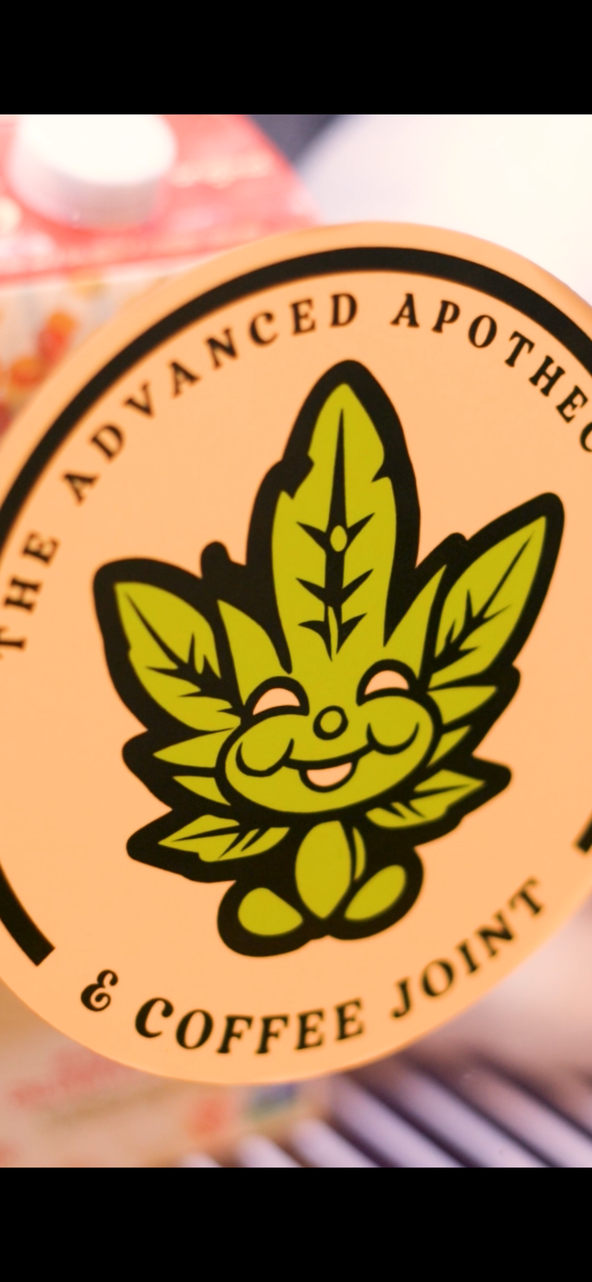 Logo featuring a smiling cartoon cannabis leaf with a face, surrounded by the text 'The Advanced Apothec & Coffee Joint'.