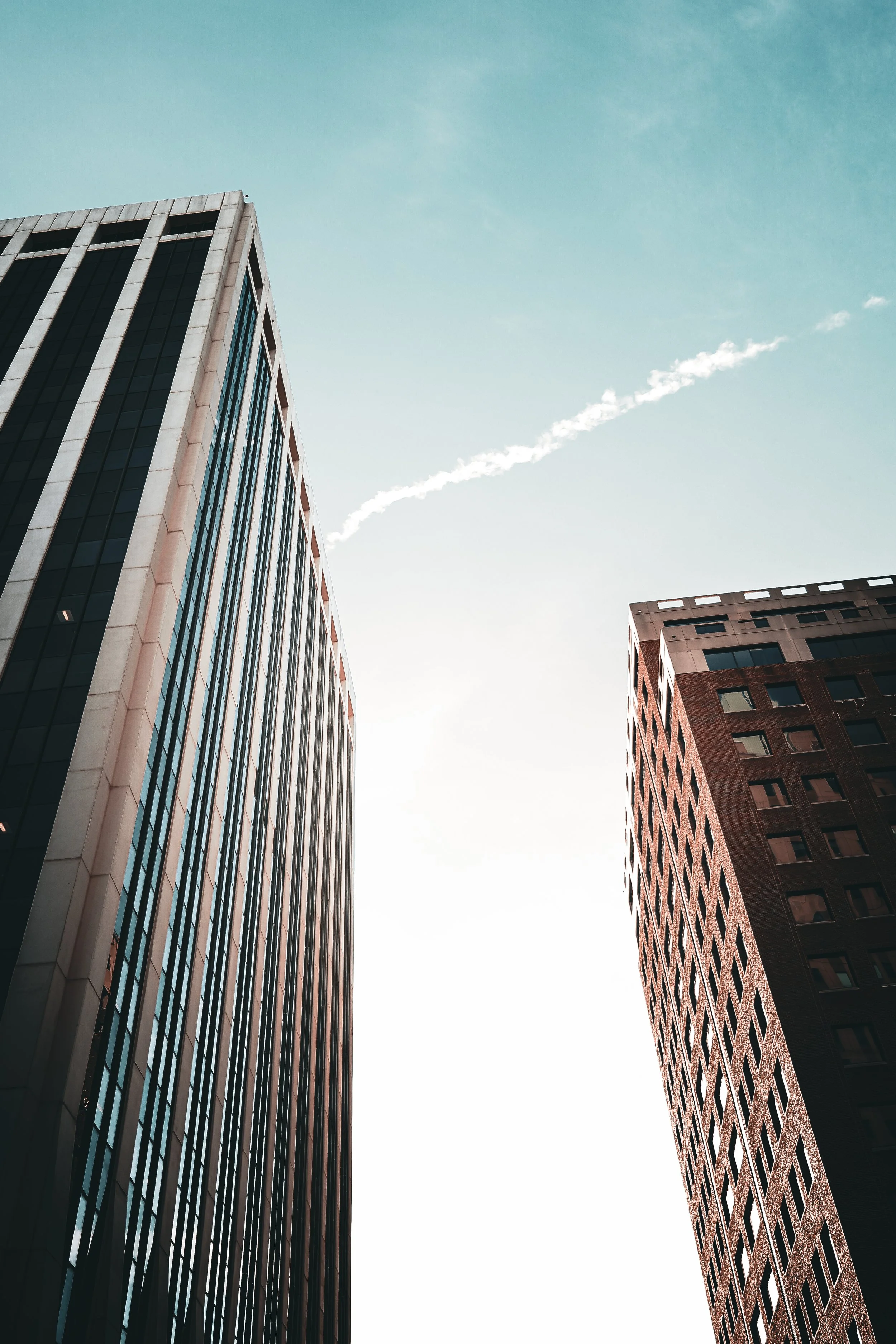Looking up at two tall office buildings against a bright sky with a puffy white cloud.