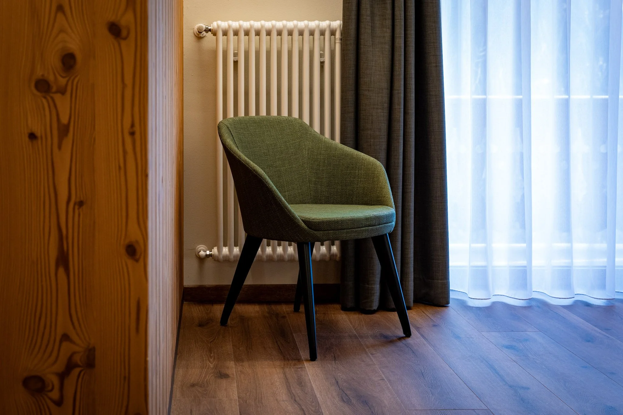 Sedia verde in un ambiente con tendaggi chiari e pareti beige, vicino a un radiatore bianco e a una porta di legno