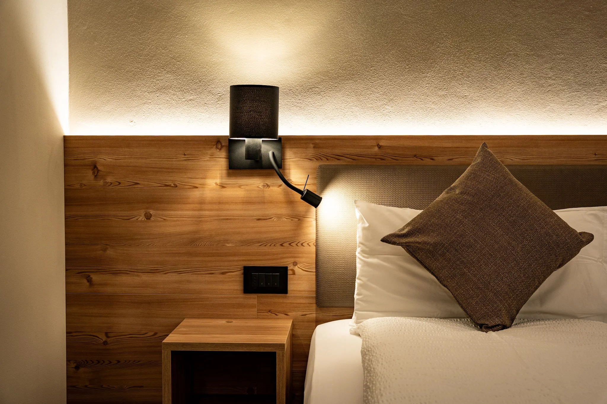 Letto con cuscino marrone e parete in./pannello di legno, lampada da muro nera con luce diffusa