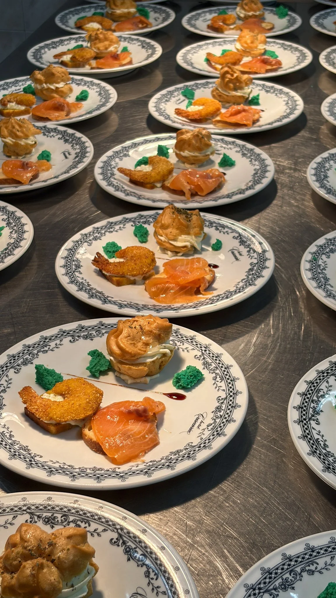 Piatti con assaggi di salmone affumicato, nachos e decorazioni verdi su piatti bianchi decorati con un motivo nero.