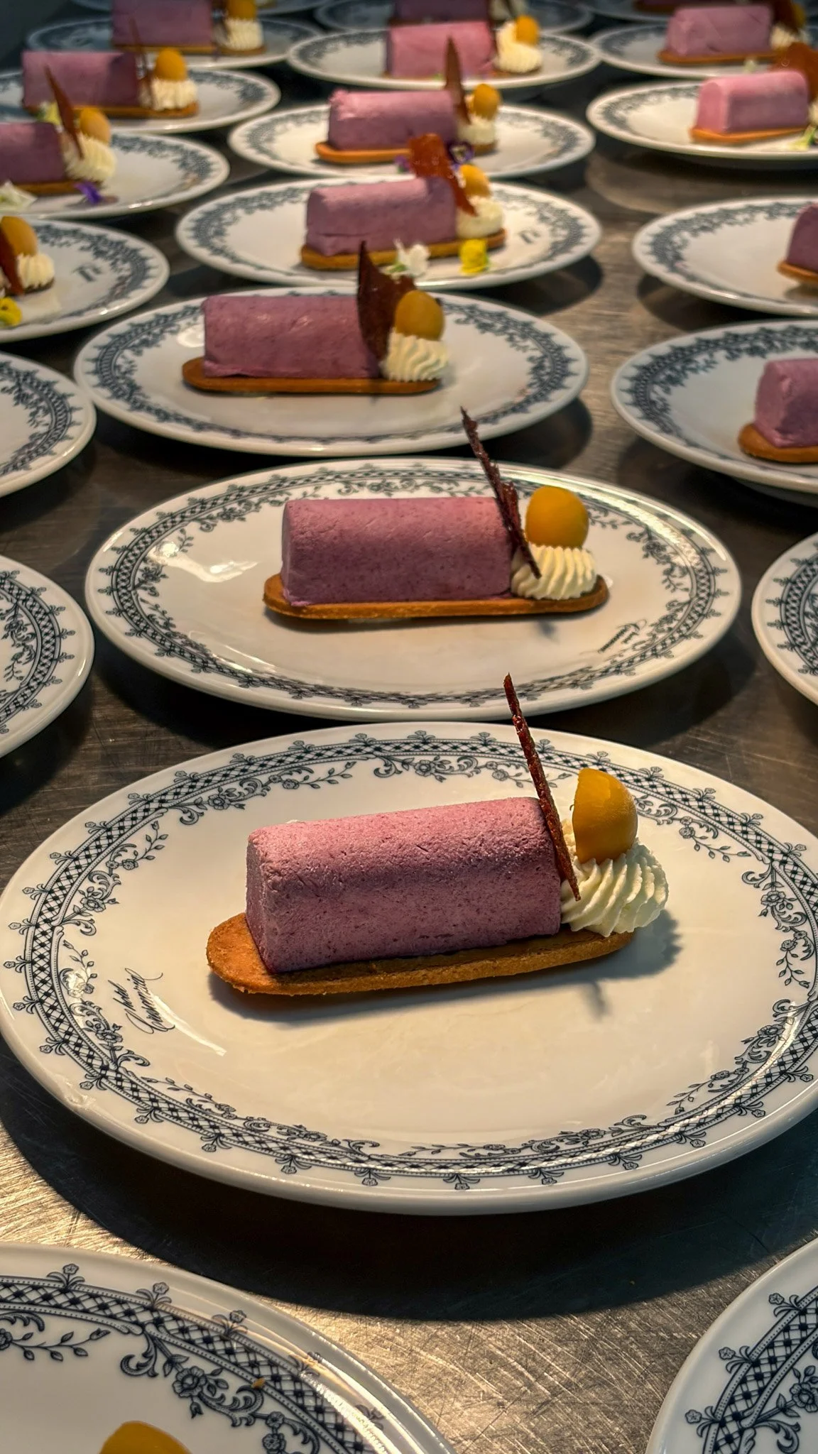 Dessert a forma di cilindro rosa su una base di biscotto, decorato con panna, una fetta di pesca e una piccola decorazione di cioccolato