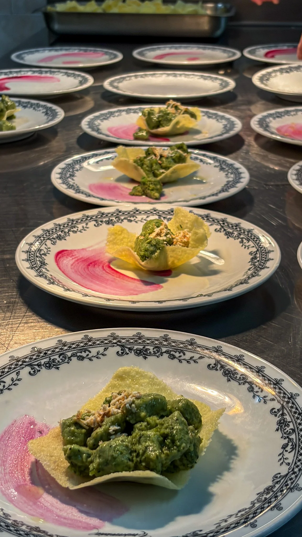 Piatti con spargola di insalata verde, posizionati su piatti decorati con un bordo colorato di nero e rosa, disposti su una superficie di colore scuro.