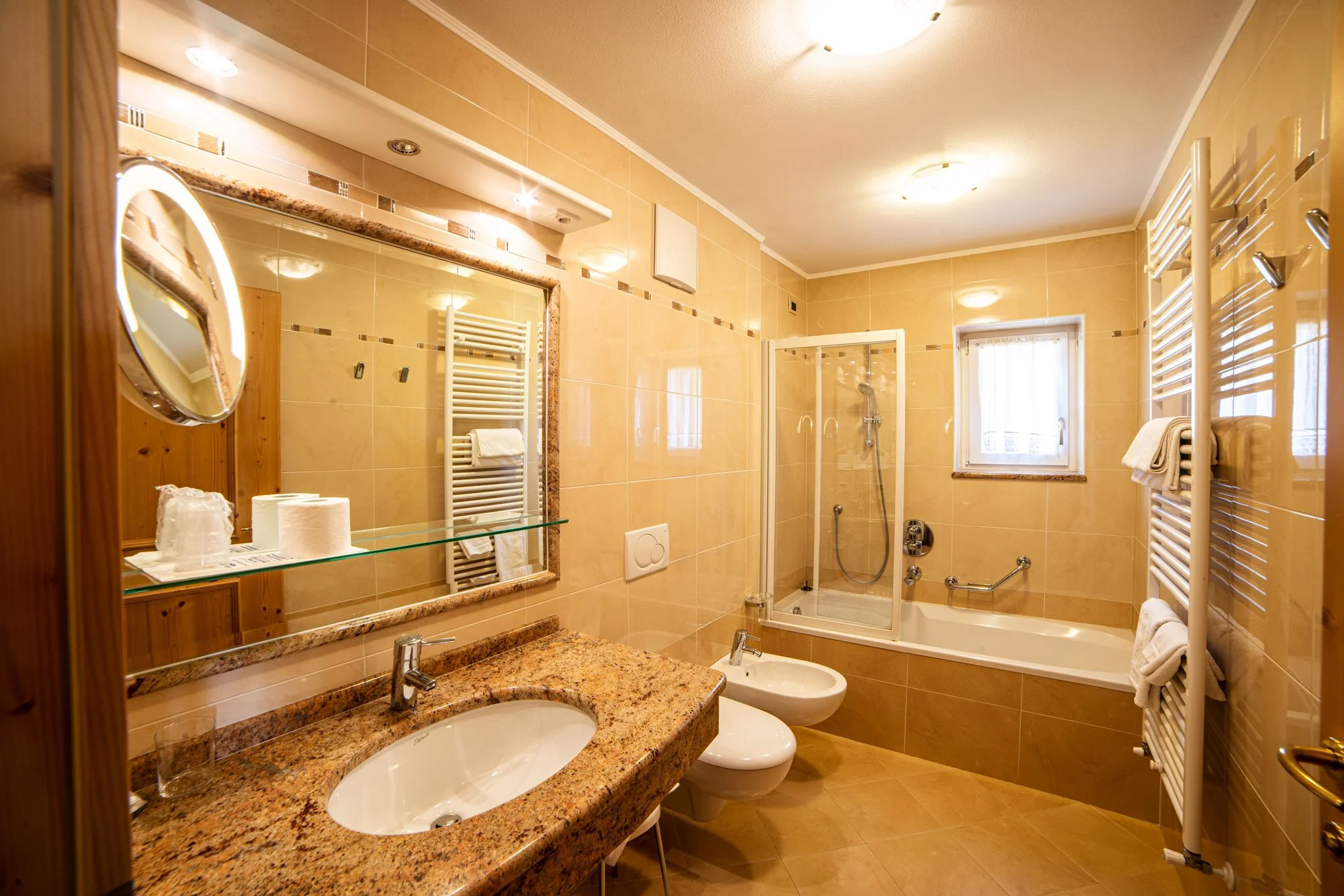 Bagno con lavabo, specchio, sanitario, box doccia, scaldasalviette e finestra.