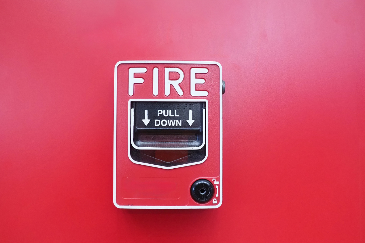 Red fire alarm pull station with white and black label that says "FIRE" and "PULL DOWN", mounted on a red wall.