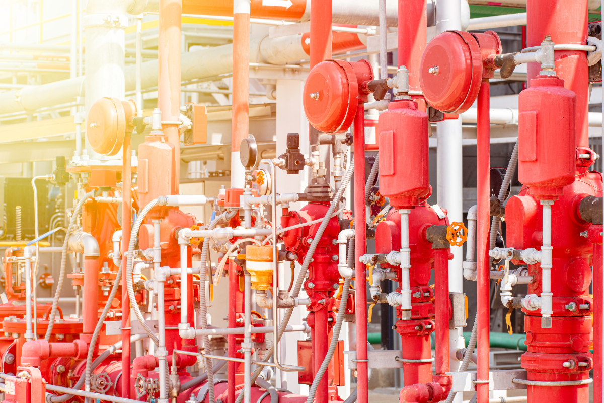 A network of industrial pipes and valves, mostly painted red and white, in an industrial setting.