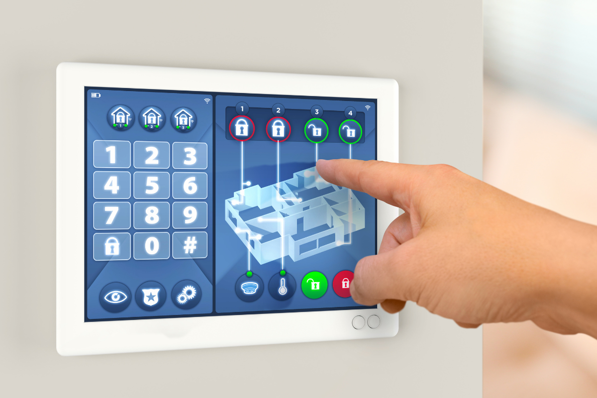 A person interacts with a digital touchscreen control panel for a smart home security system, displaying a 3D house layout, security status icons, and control buttons.
