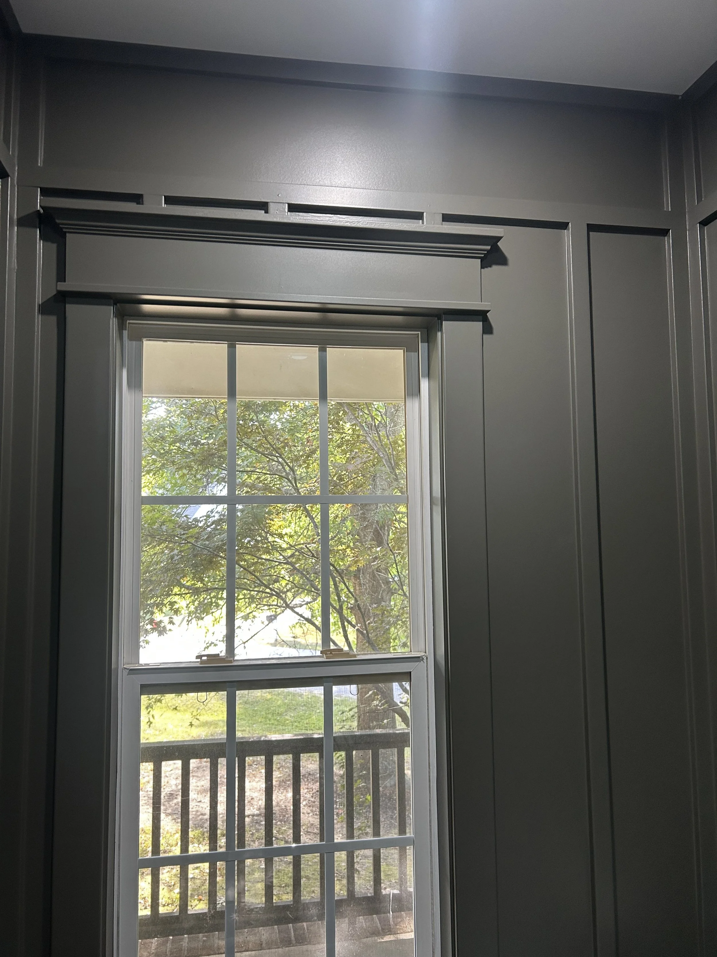 Interior view of a window with a gray wooden frame, showing trees and grass outside through the glass.