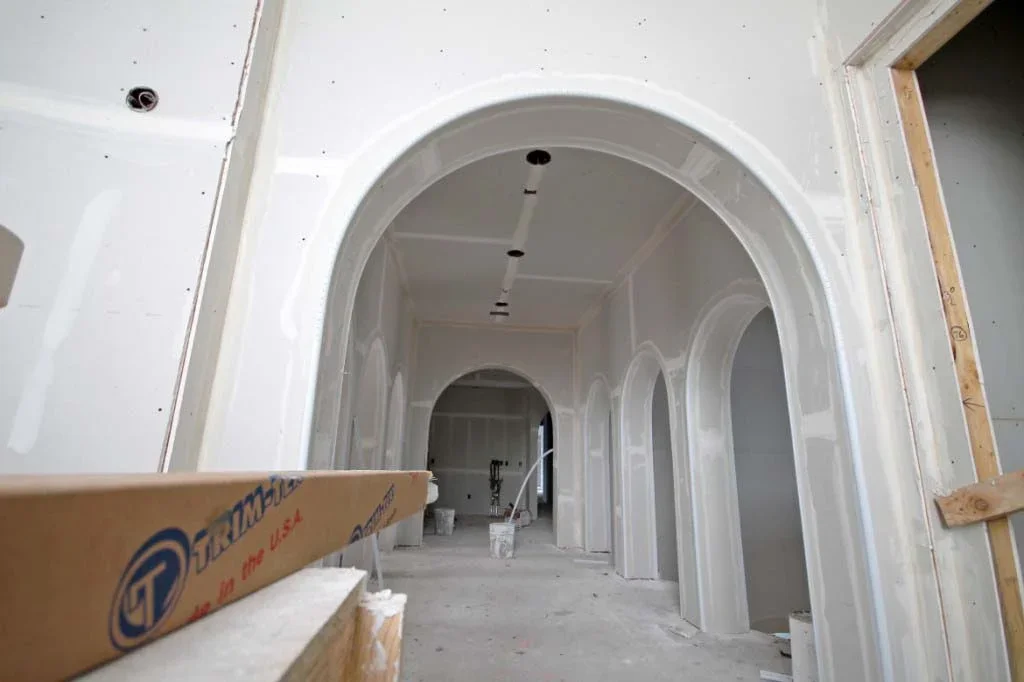 Interior view of a building under construction, showing unfinished walls with archways, exposed wiring, and construction materials.