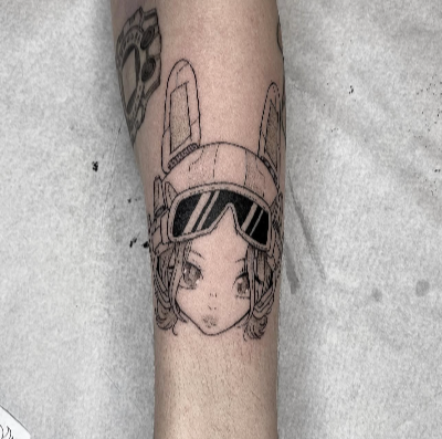 Tattoo of a young girl wearing a pilot helmet and goggles on a forearm.