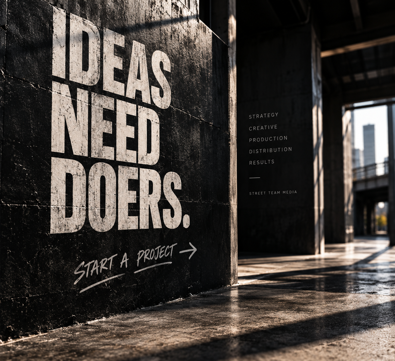 A black wall with large white text saying 'IDEAS NEED DOERS.' and smaller text underneath saying 'START A PROJECT' with an arrow. To the right, there is a list including 'STRATEGY,' 'CREATIVE,' 'PRODUCTION,' 'DISTRIBUTION,' 'RESULTS,' and 'STREET TEAM MEDIA.' The photo is taken outdoors in an urban setting with sunlight and buildings in the background.