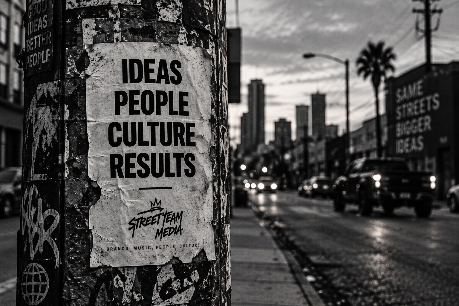 Street scene in black and white with a poster on a pole that reads 'Ideas People Culture Results' and the words 'Street Team Media' underneath. City buildings, cars, and a palm tree are visible in the background.