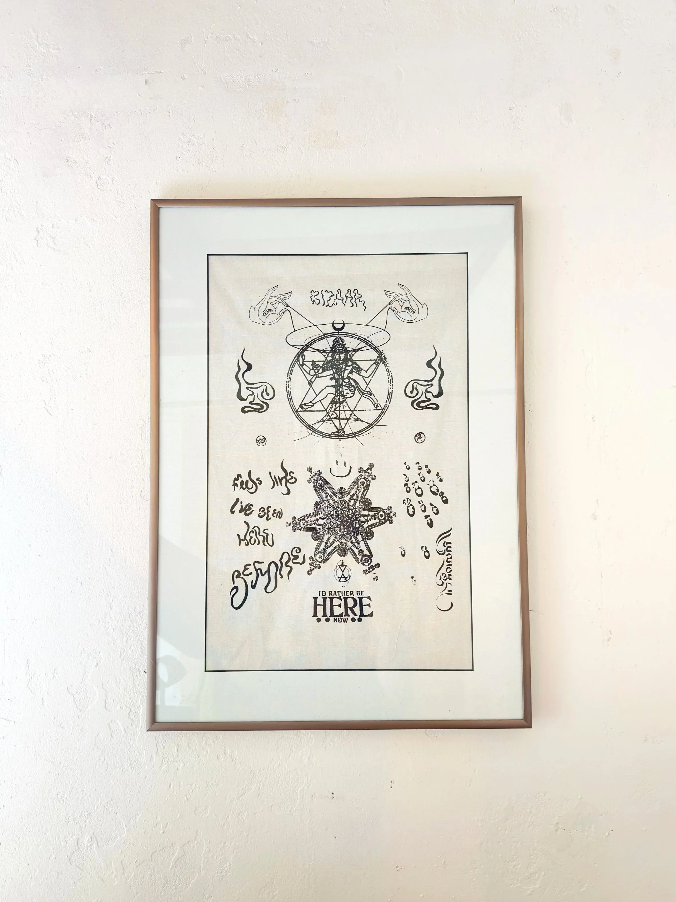 Framed black and white artistic drawing of geometric and abstract symbols, including a dancing shiva, surrounded by text and various artistic elements, hanging on a white wall.