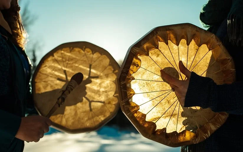 Two people holding decorative amber-colored drums outdoors with a bright sky in the background.