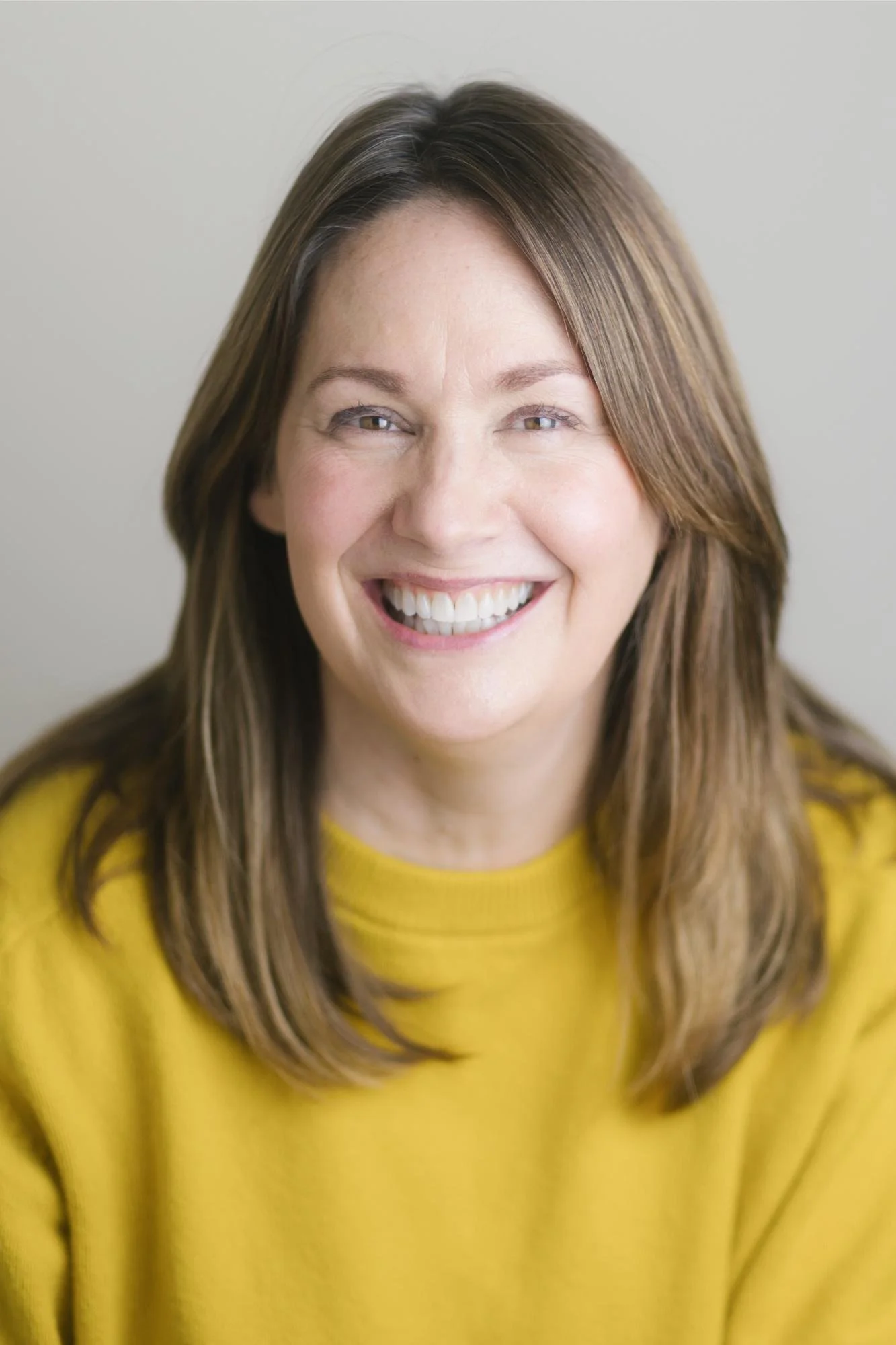 Close-up photo of a woman with brown hair wearing a yellow top, smiling at the camera.