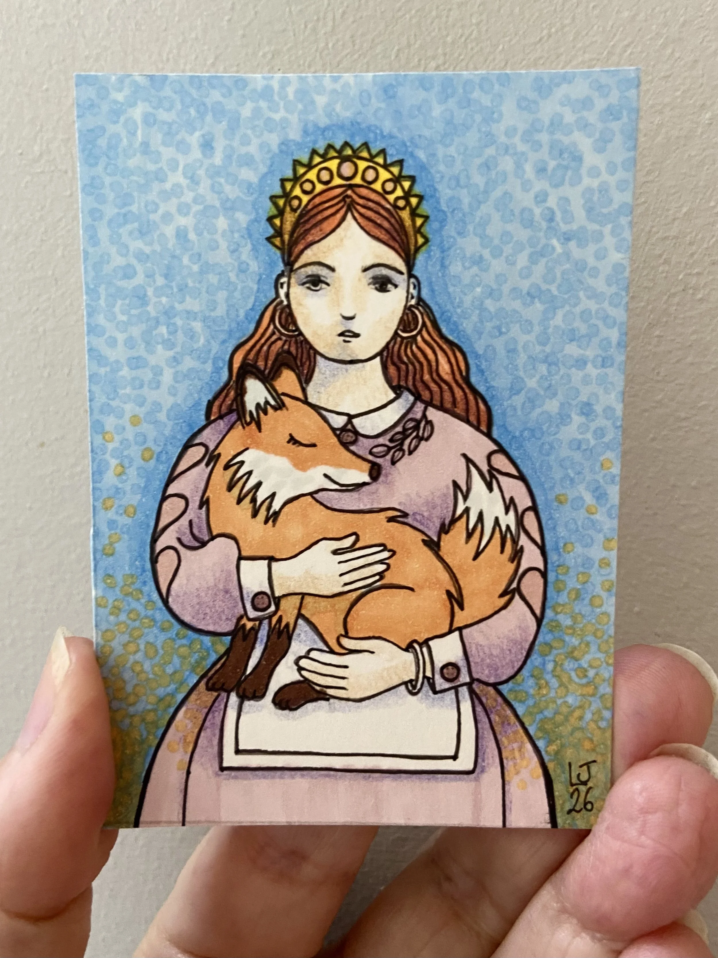 A hand holding a colorful drawing of a woman with red hair, a crown, and a purple cloak, holding a fox in her arms against a blue patterned background.