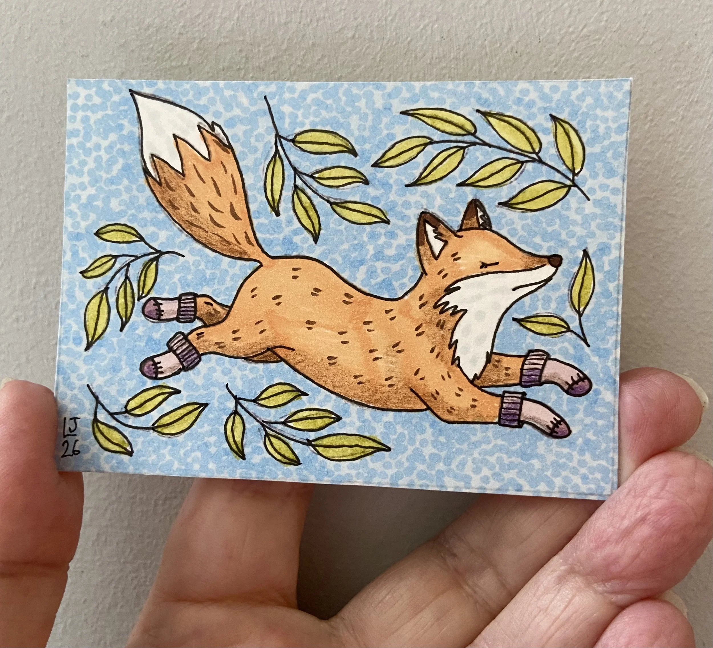 Drawing of a fox wearing socks running with leaves around it on a blue patterned background, held in person's hand.