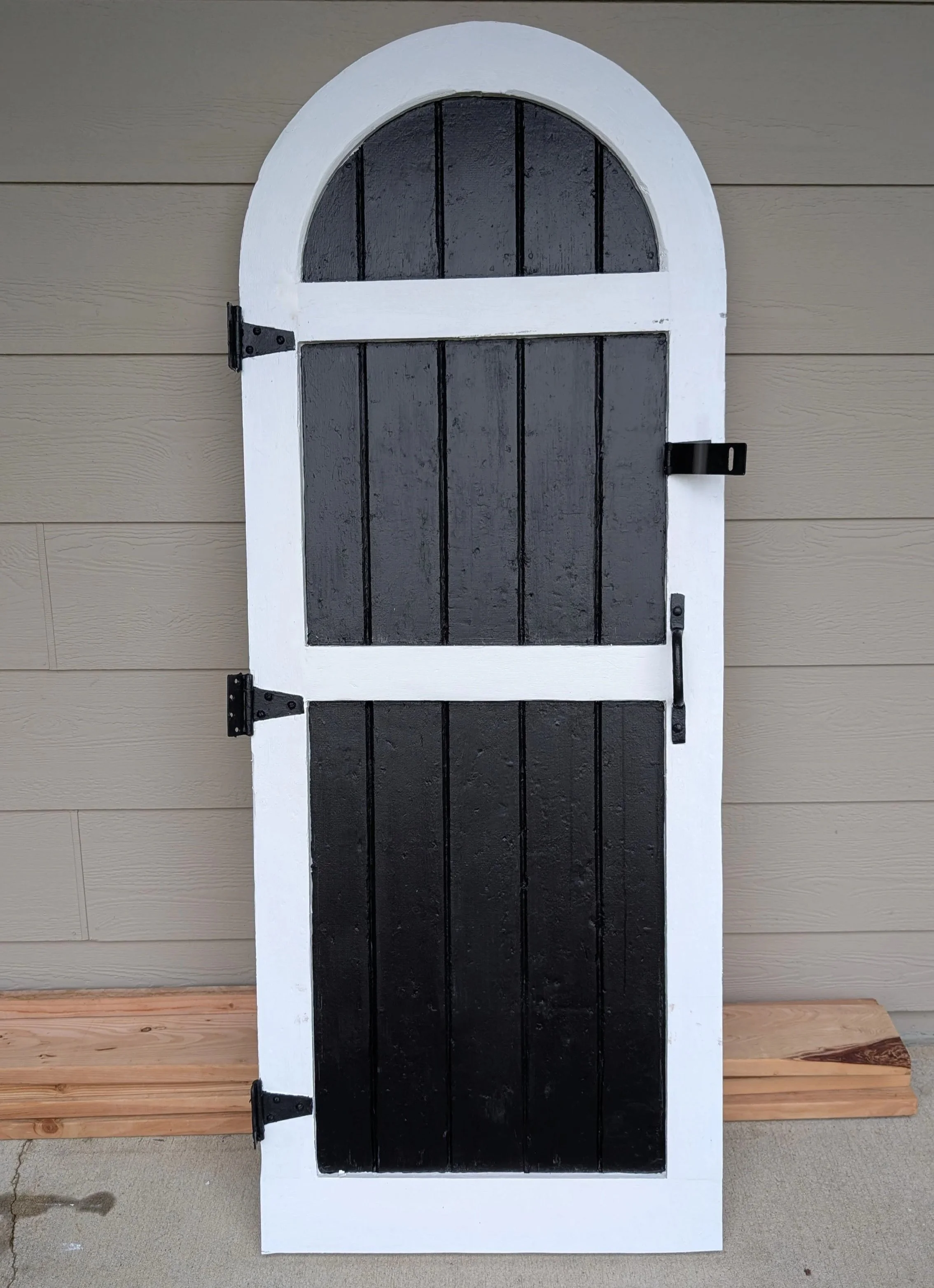 Small window with black shutters, white frame, and black hardware, mounted on a beige exterior wall, with wooden bench below.