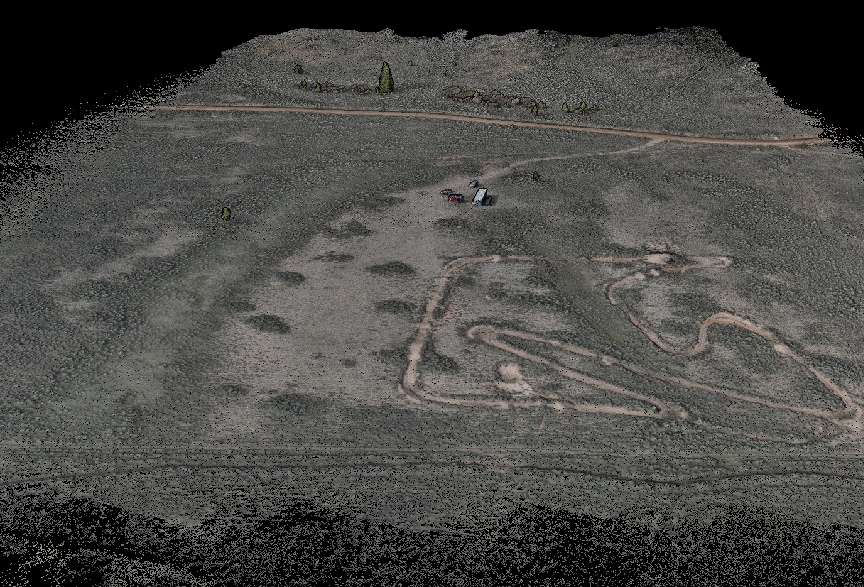 Drone view of vast open landscape with multiple dirt roads, sparse vegetation, a small cluster of vehicles, and a large word 'LOVE' spelled out in the dirt.