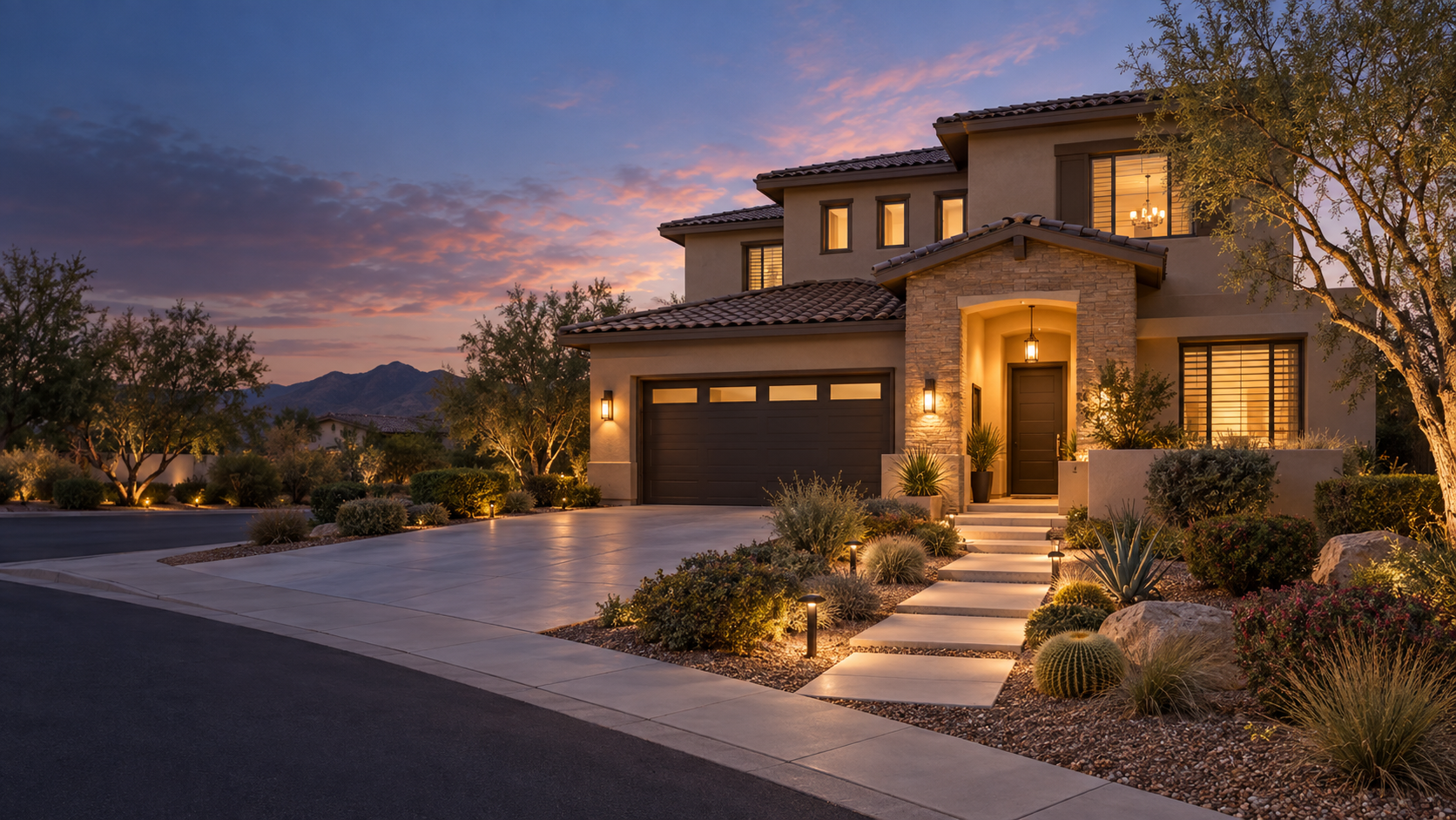 Modern two-story house at dusk with a landscaped front yard, illuminated pathway, and mountain range in the background.