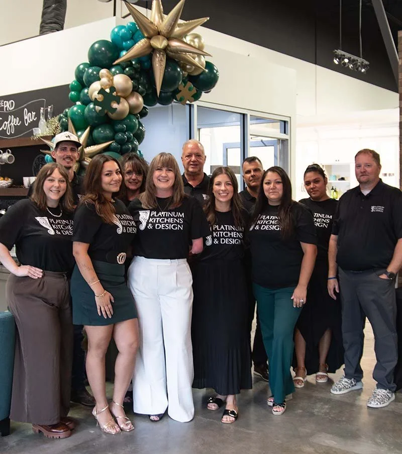 Platinum Kitchens & Design team posing beneath a green, gold, and teal balloon arch with a starburst decoration.