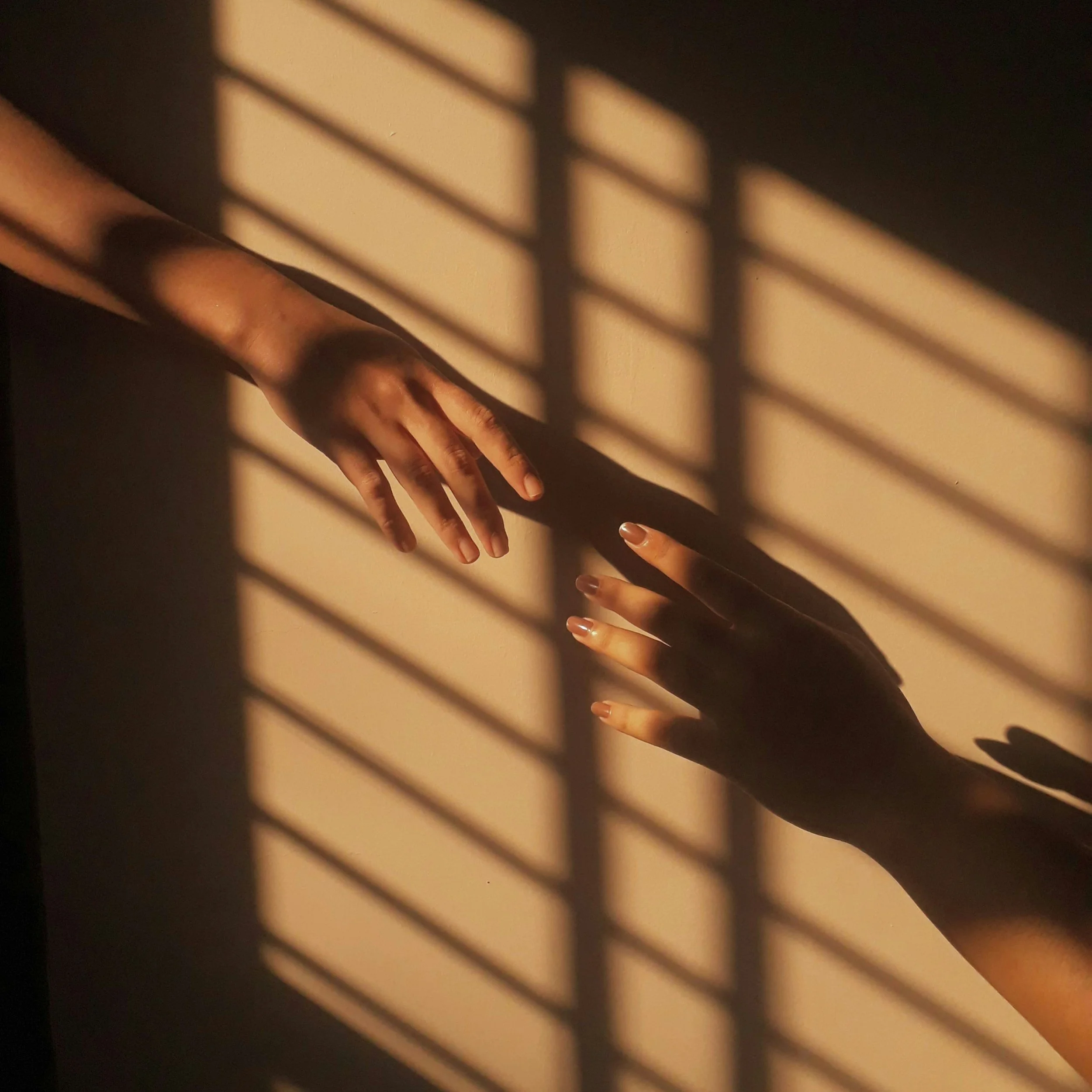 Shadow patterns of a window with horizontal slats cast on the surface near a hand.