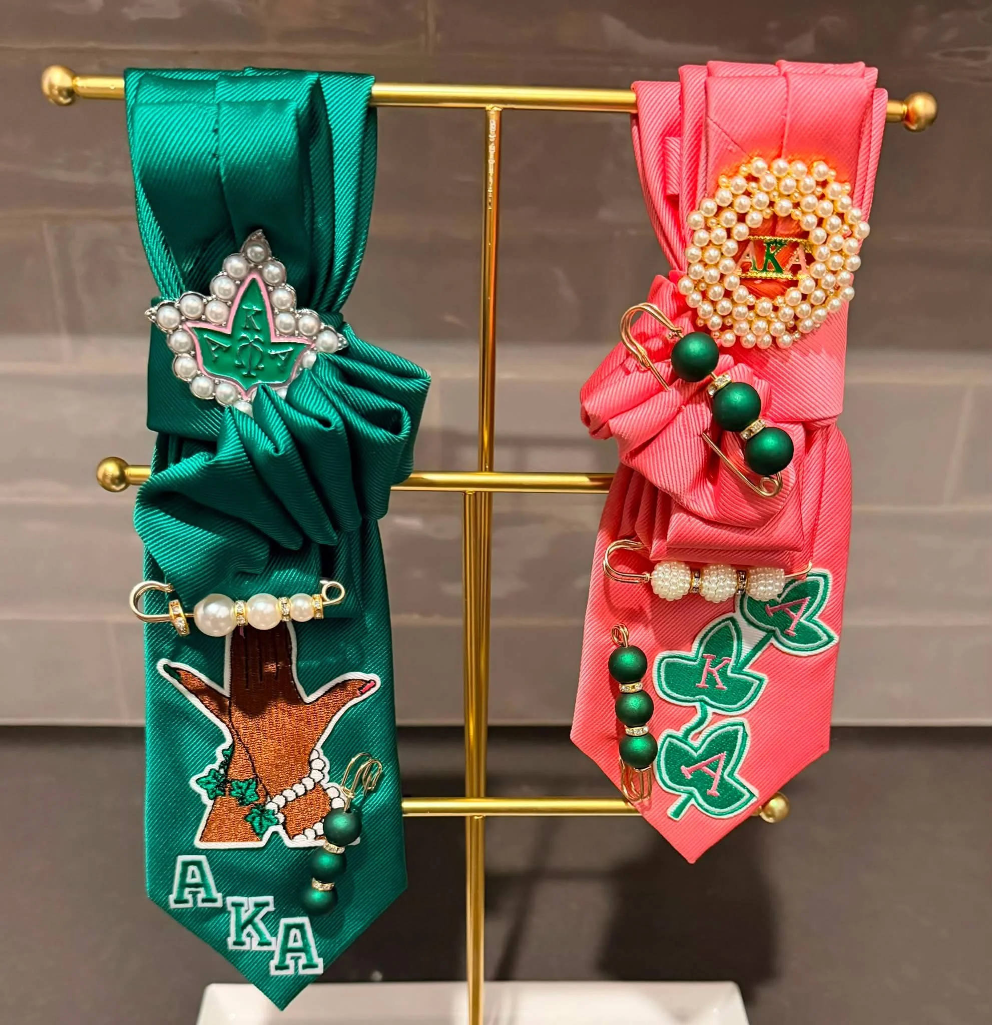 Two decorative ribbons, one green and one pink, are adorned with pearl-like beads, gold accents, and messages for graduation. The green ribbon features a frog with the word 'Aloha,' and the pink ribbon features a shamrock with the word 'Luck.'