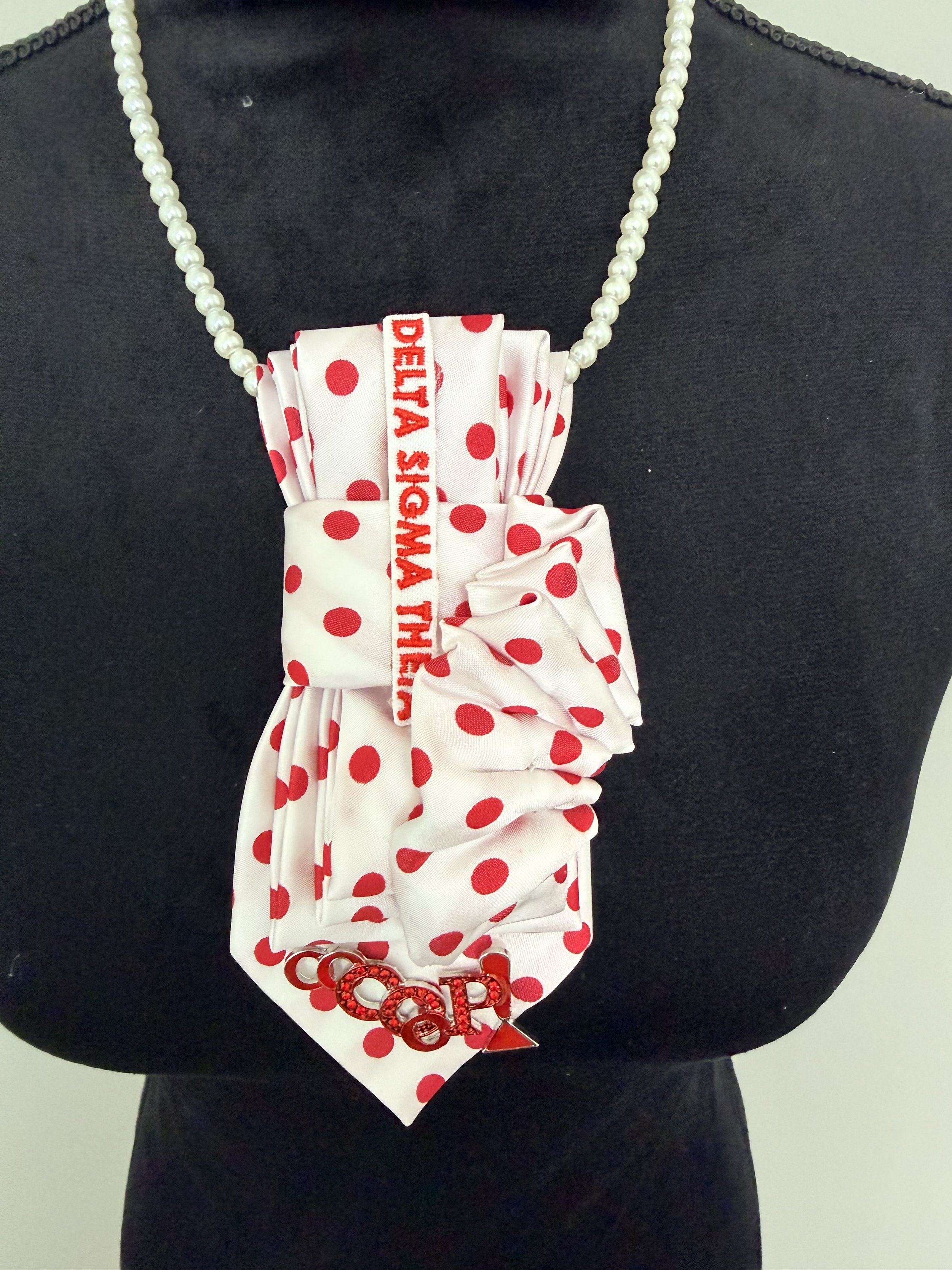 A black mannequin wearing a white and red polka-dotted fabric bow with a pearl necklace and a red 'LOVE' accessory.