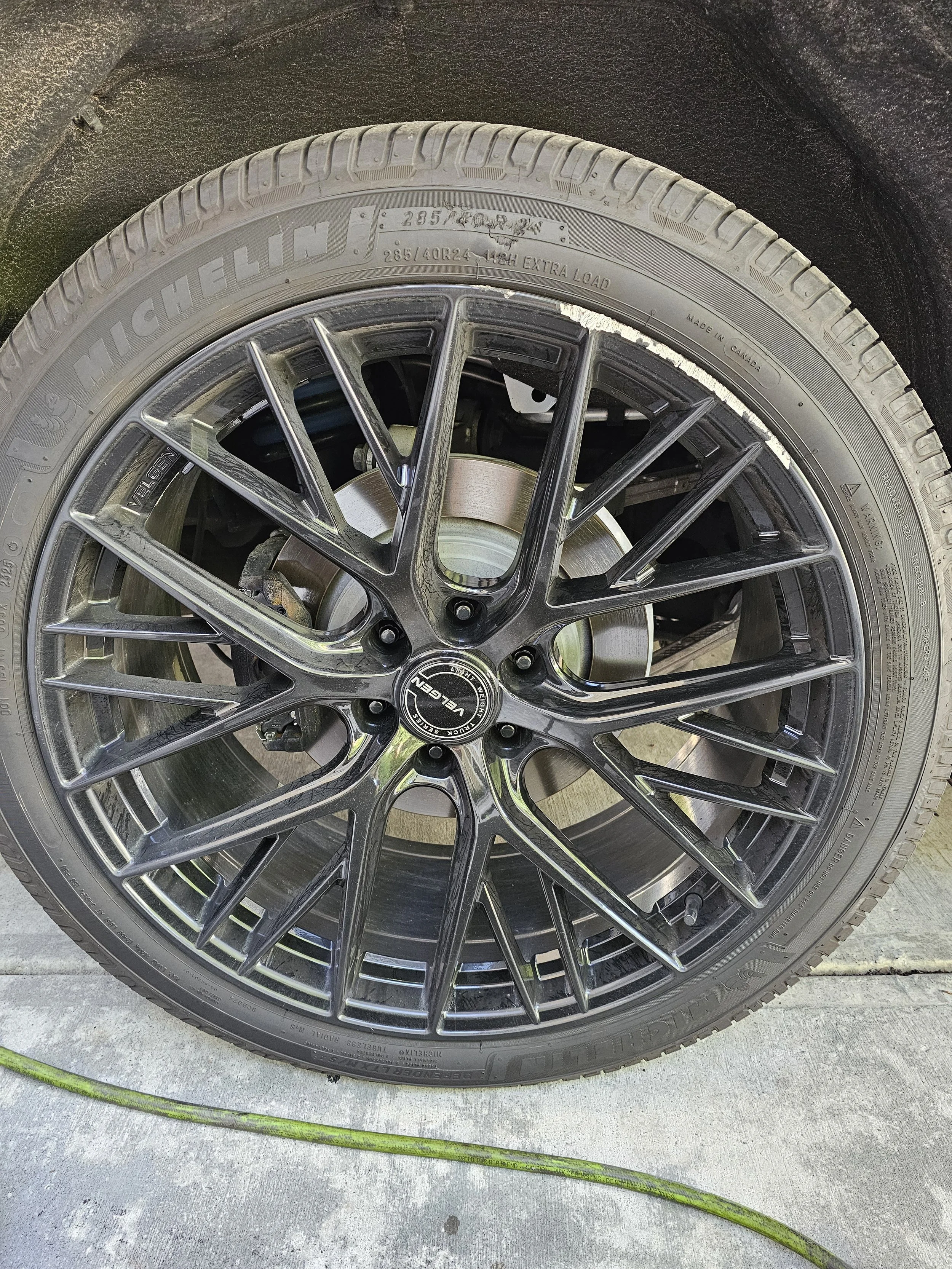 Close-up of a damaged car wheel with curb scuffs featuring a black and silver alloy rim with a low-profile Michelin tire mounted.
