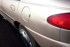 Close-up of a crease in a beige Ford sedan, focusing on the rear side including the taillight and wheel.