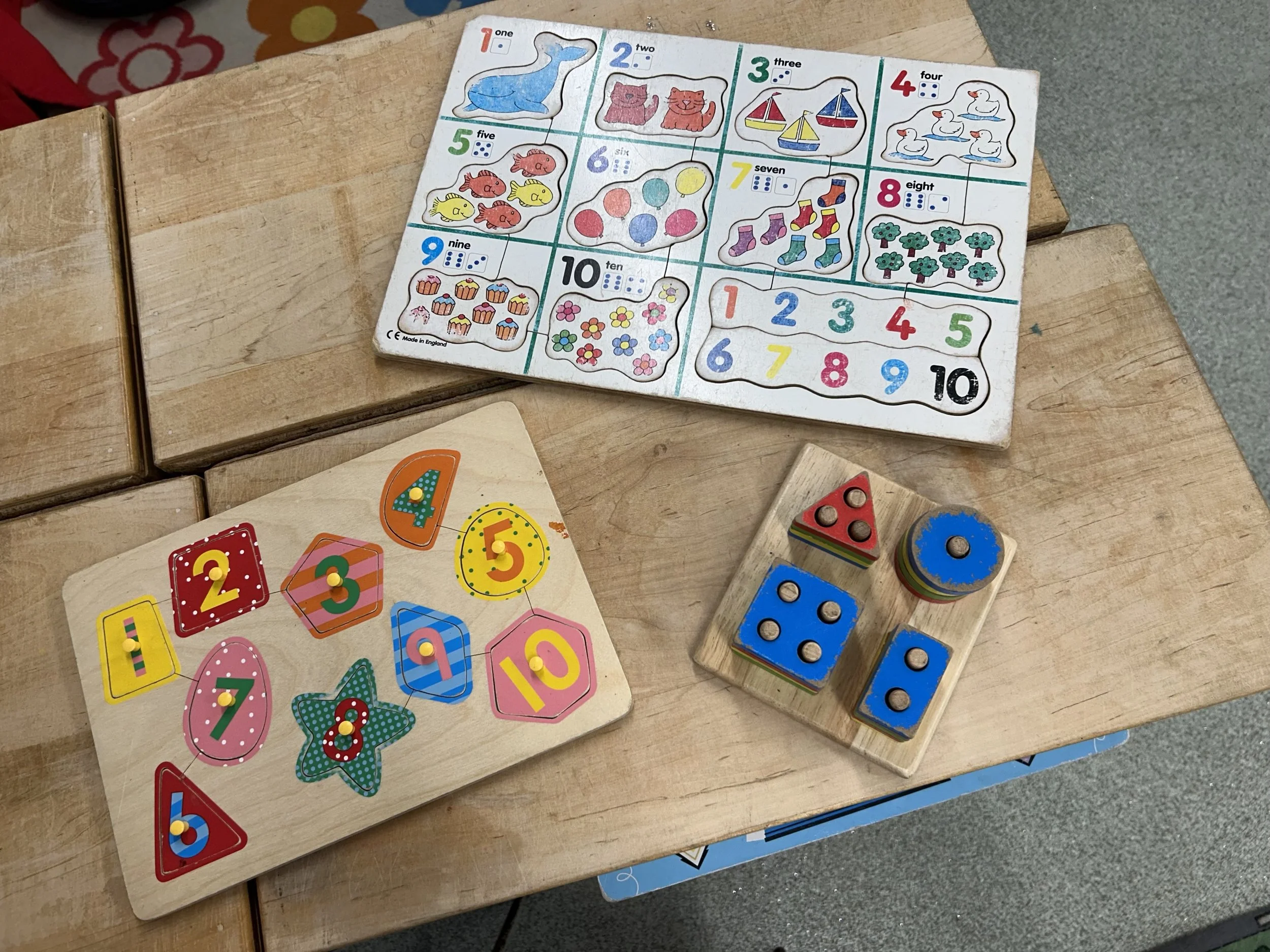 Colorful educational toys on a wooden table, including a card with animals and numbers from one to ten, and another card with colorful numbered shapes.