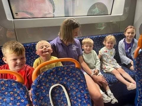 Group of children and a woman sitting on a bus, smiling and looking at the camera.