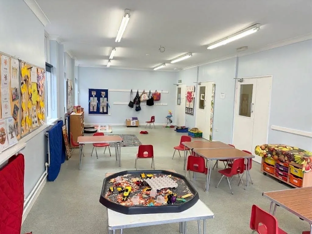 Empty classroom with red chairs, tables, and toy box, decorated with children's artwork on walls