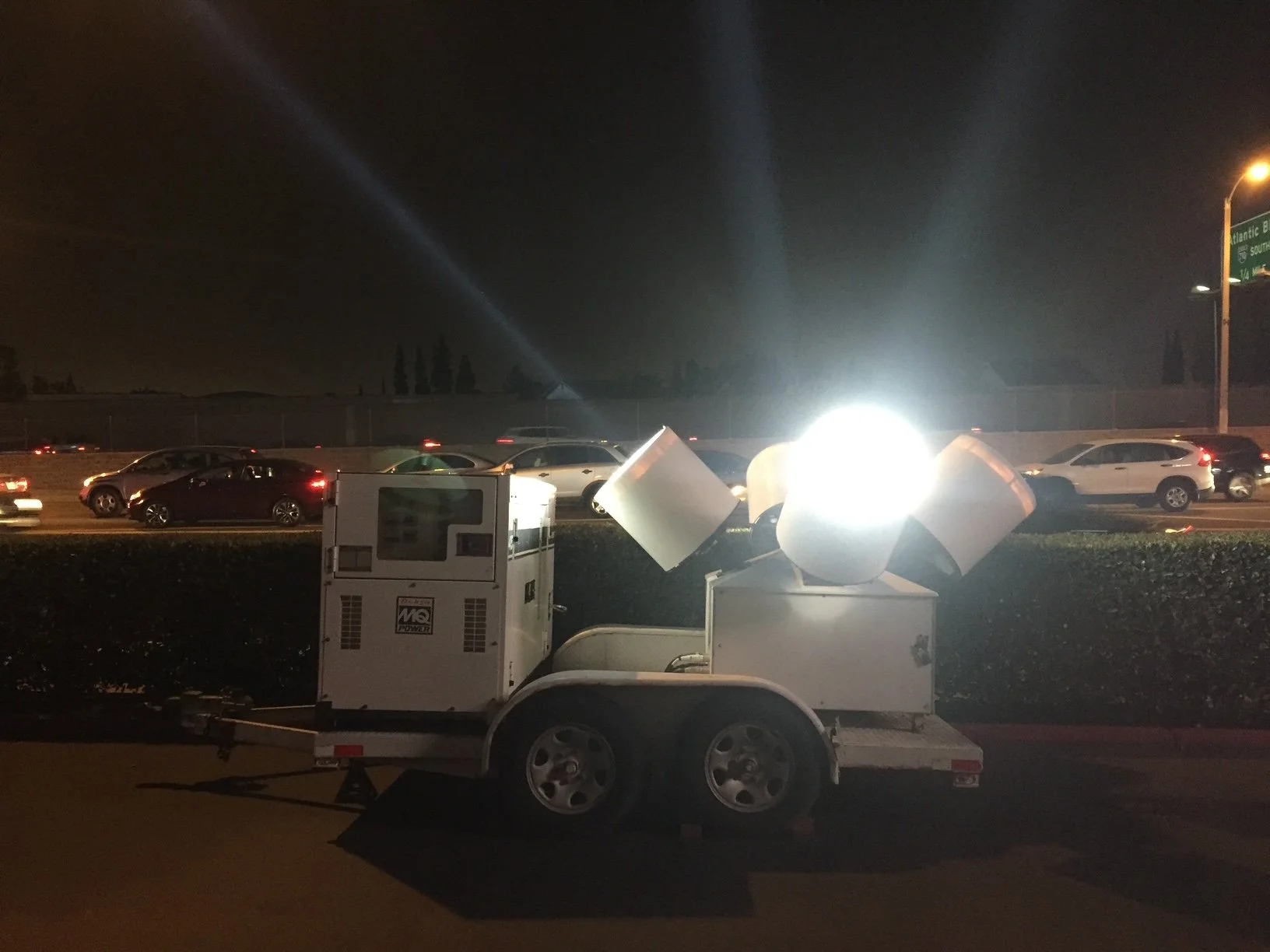 A portable generator on a trailer is use to power streetlights that are turned on. The scene is dark, with cars on a highway in the background.