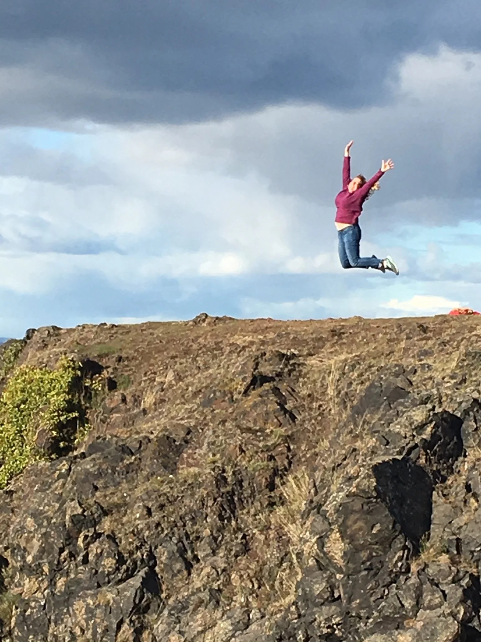 A person mid-jump on rocky terrain outdoors, with a cloudy sky in the background.