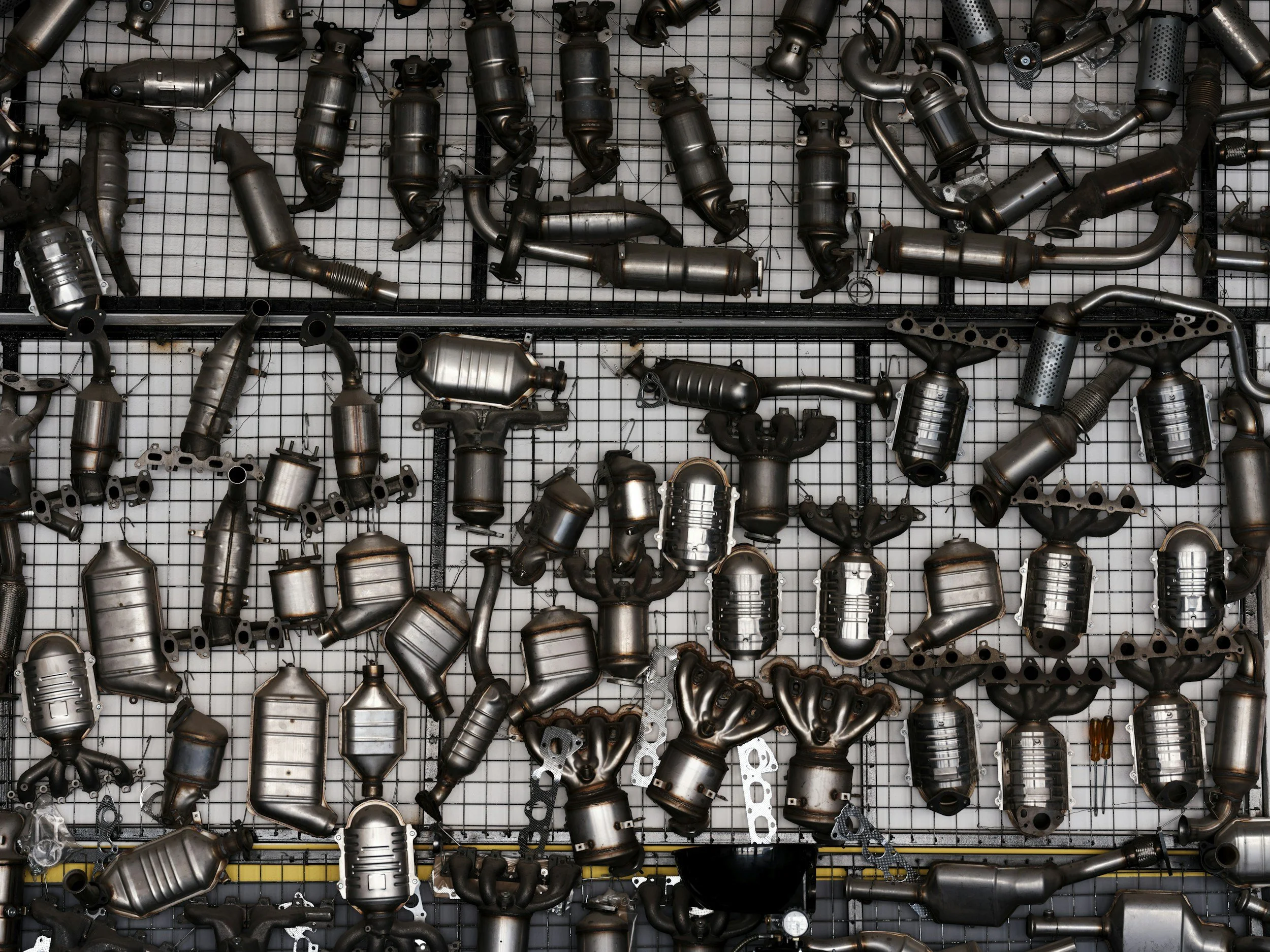 A grid wall displaying various metallic car parts, including exhaust pipes and catalytic converters.